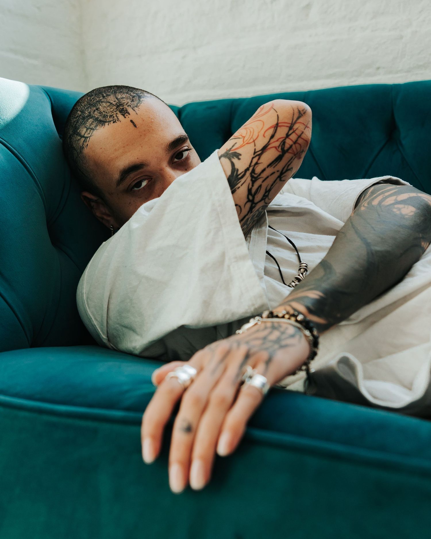Person resting on a teal couch wearing a white shirt, with focus on their tattooed hand.