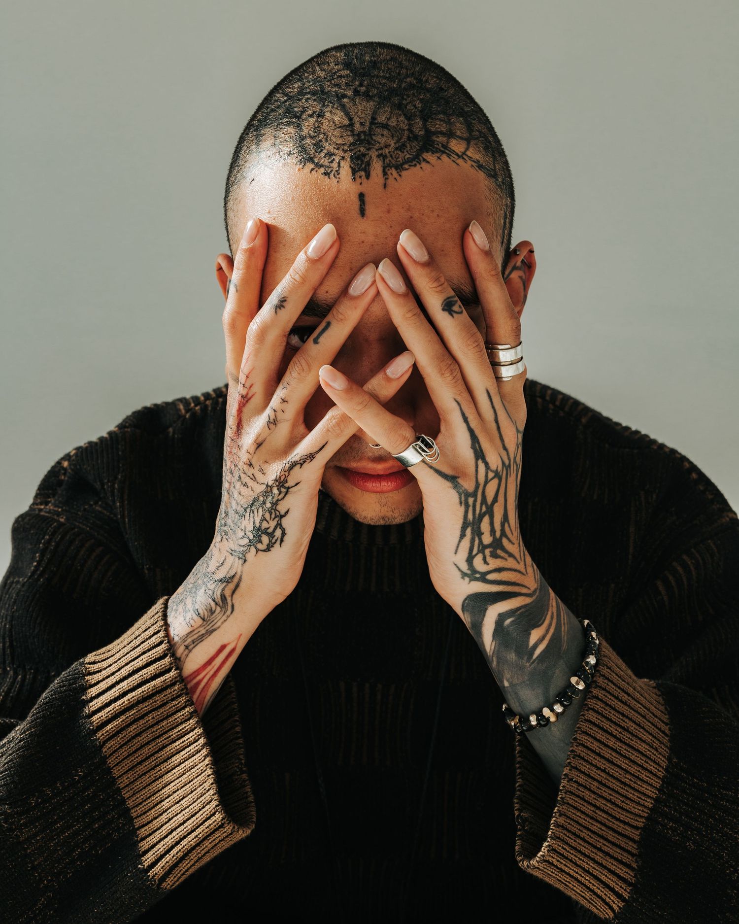 Person with tattooed hands covering their face in a sequence of artistic black and white portraits.
