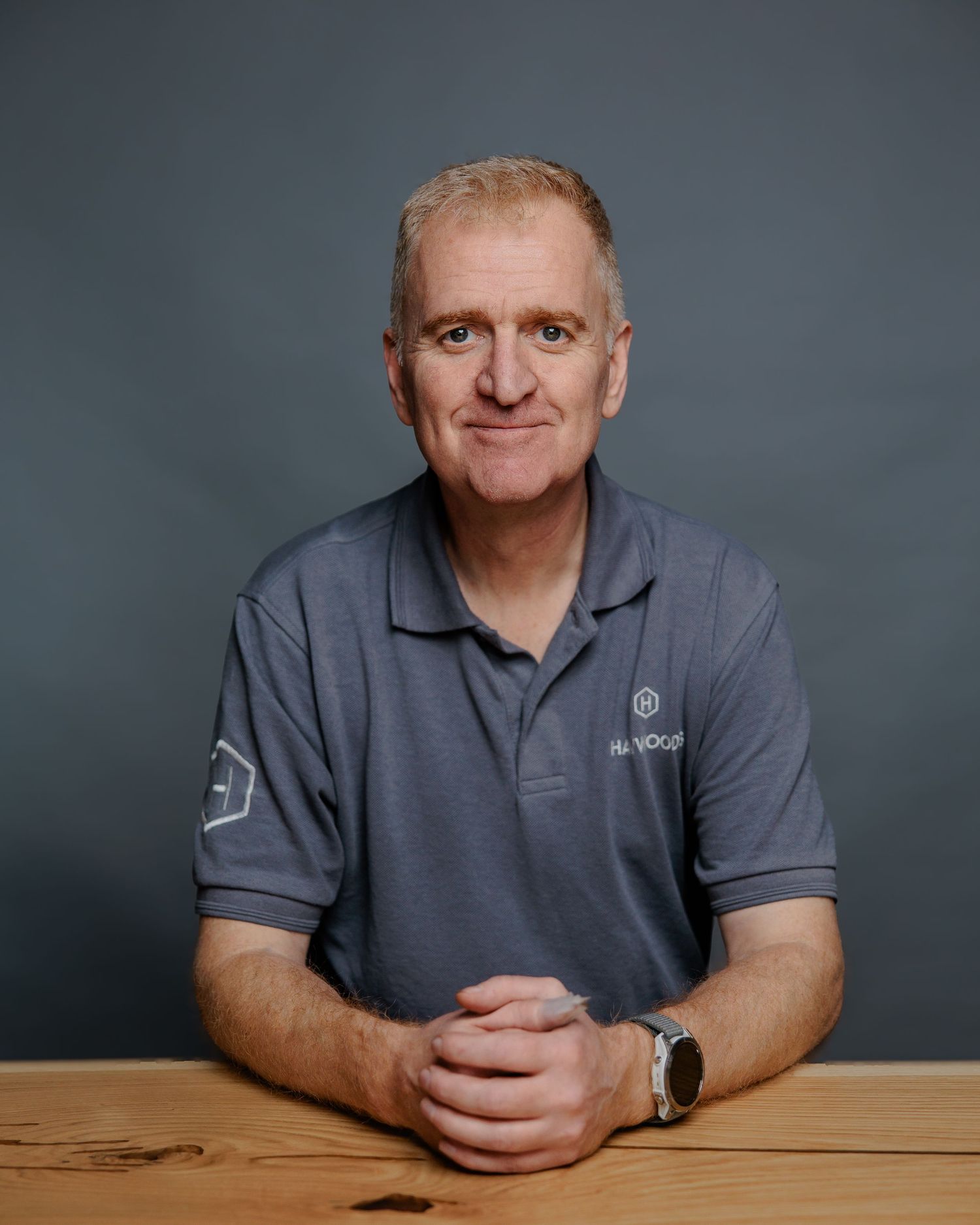 A person in a gray polo shirt sits at a wooden table against a dark background in a series of similar poses.