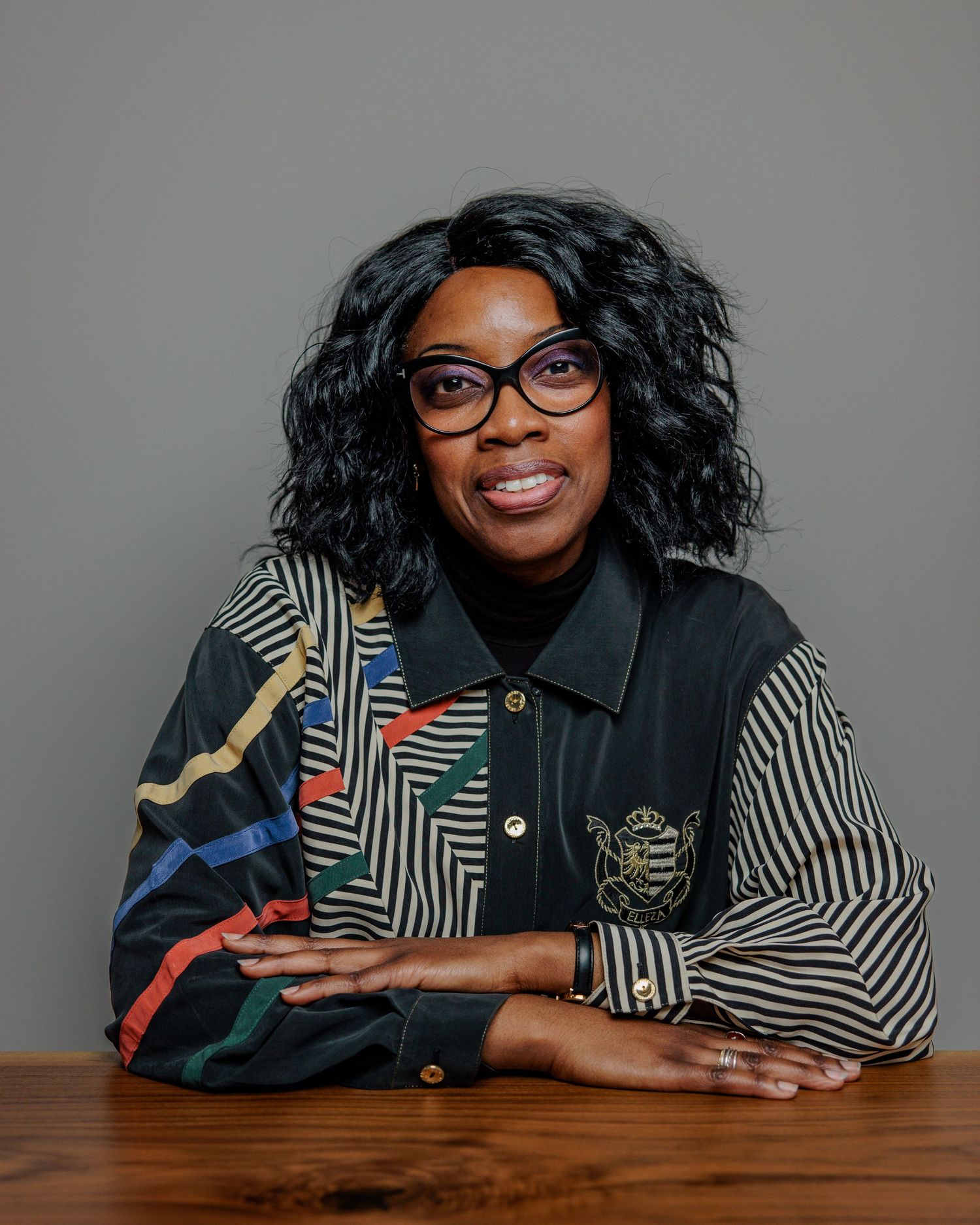 A smiling figure in glasses and striped clothing poses for a series of expressive portraits at a wooden table.