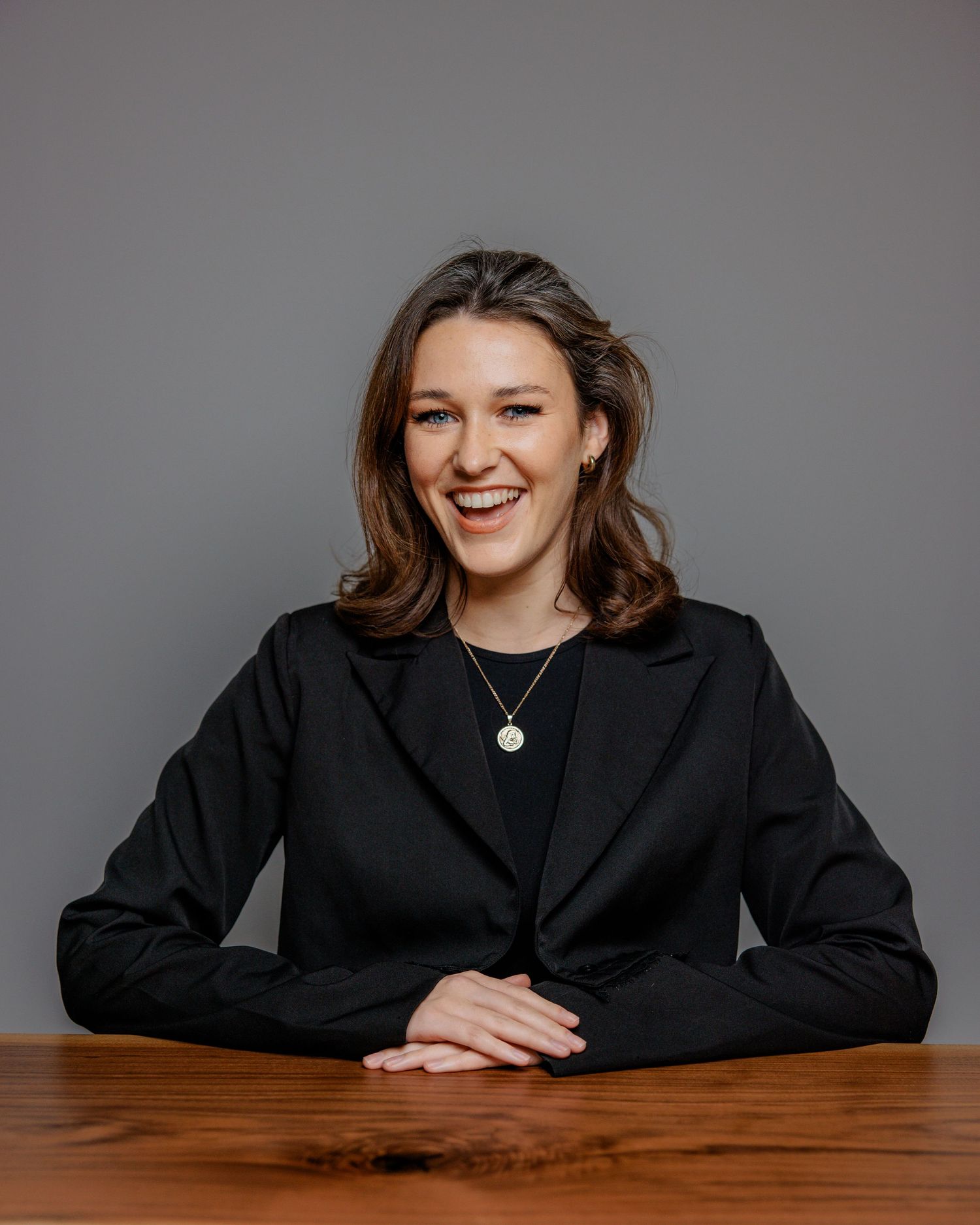 Professional portrait series showing a person in a black blazer seated at a wooden table against a gray background.