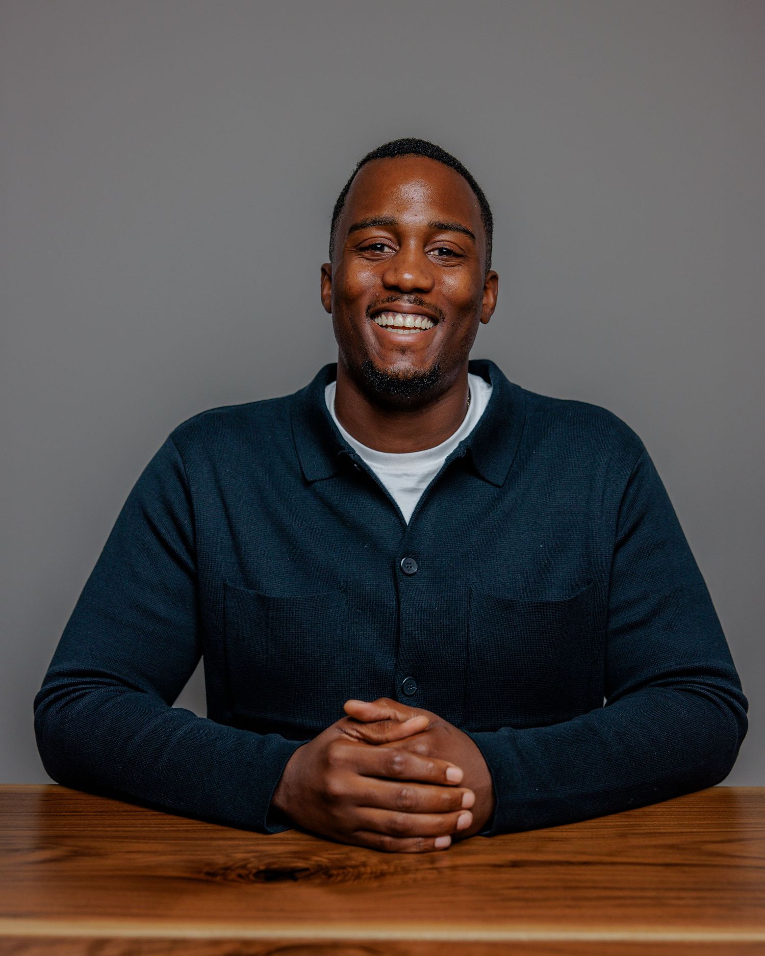 Professional wearing a dark suit jacket sits at wooden table in studio setting with warm lighting and varied expressions.