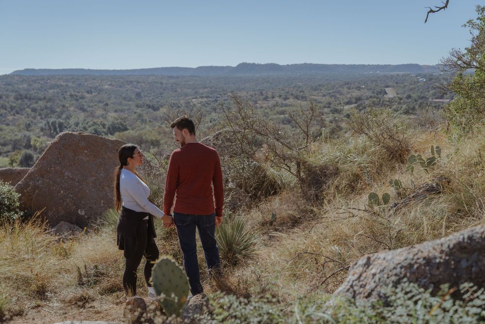 People hiking along a rocky desert trail overlooking vast mountainous terrain under clear blue skies.