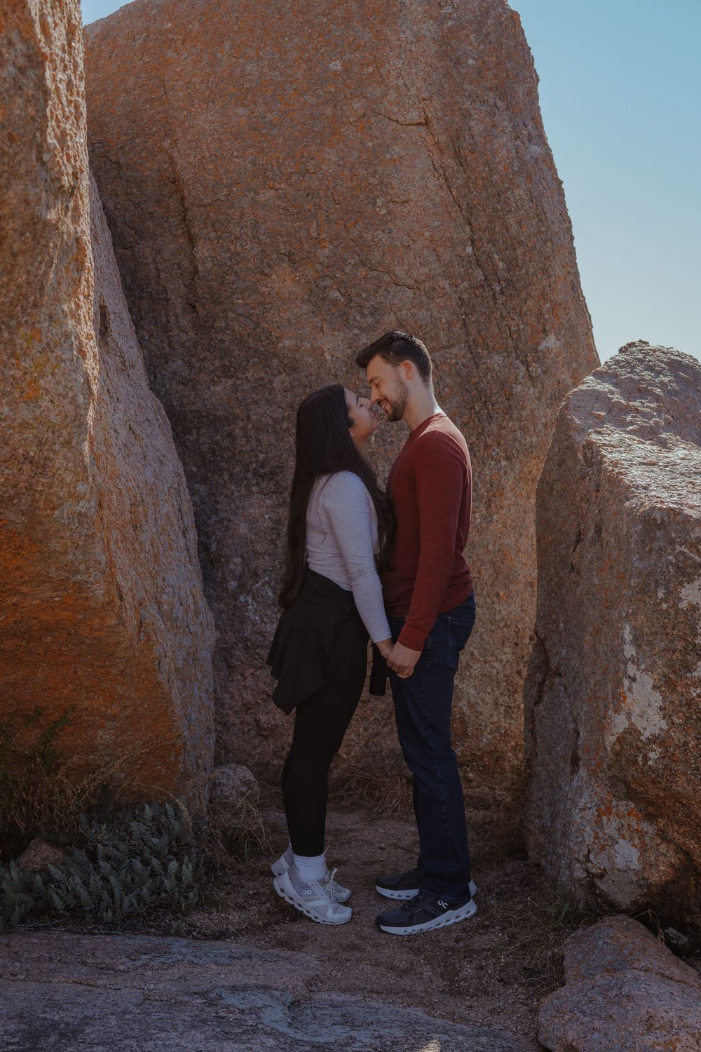 A couple shares a tender moment while standing between towering desert rock formations at sunset.