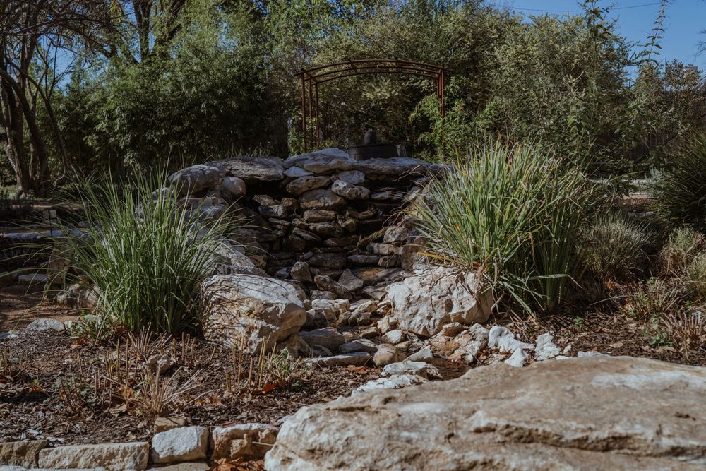 A stone pathway winds through a desert garden with native plants and decorative rocks.