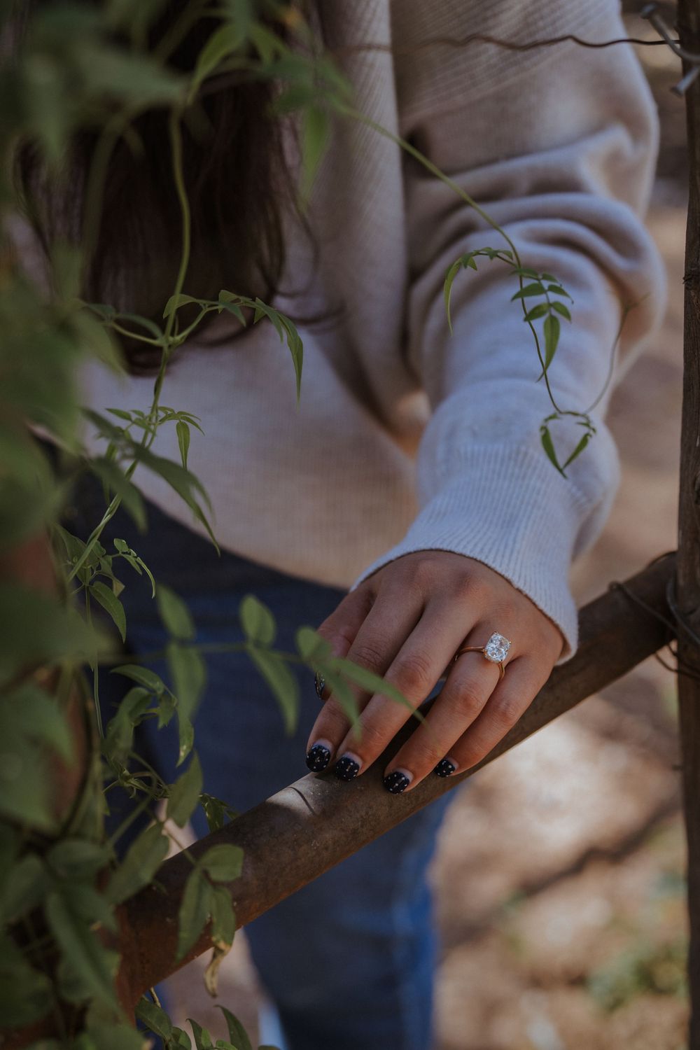 Close-up shots of hands with black nail polish gently touching green plant vines in soft natural lighting.