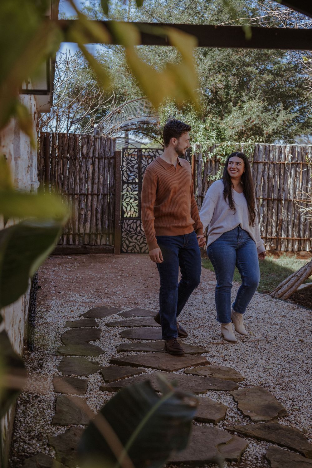 A couple sits together on stone steps in a rustic outdoor garden setting with a wooden fence in the background.