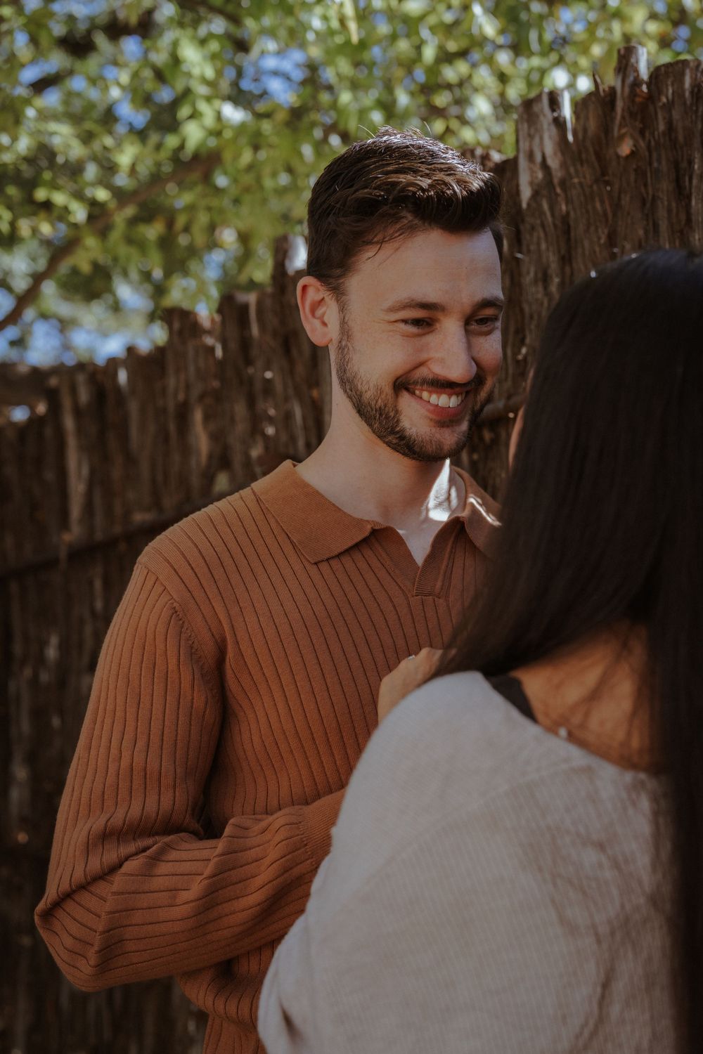 Romantic couple sharing intimate moments outdoors against wooden fence in warm autumn lighting.