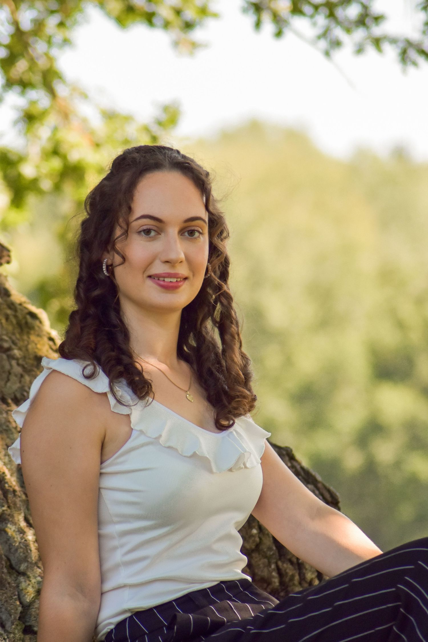 Portrait of someone in a white ruffled top sitting against a rock in a natural outdoor setting.