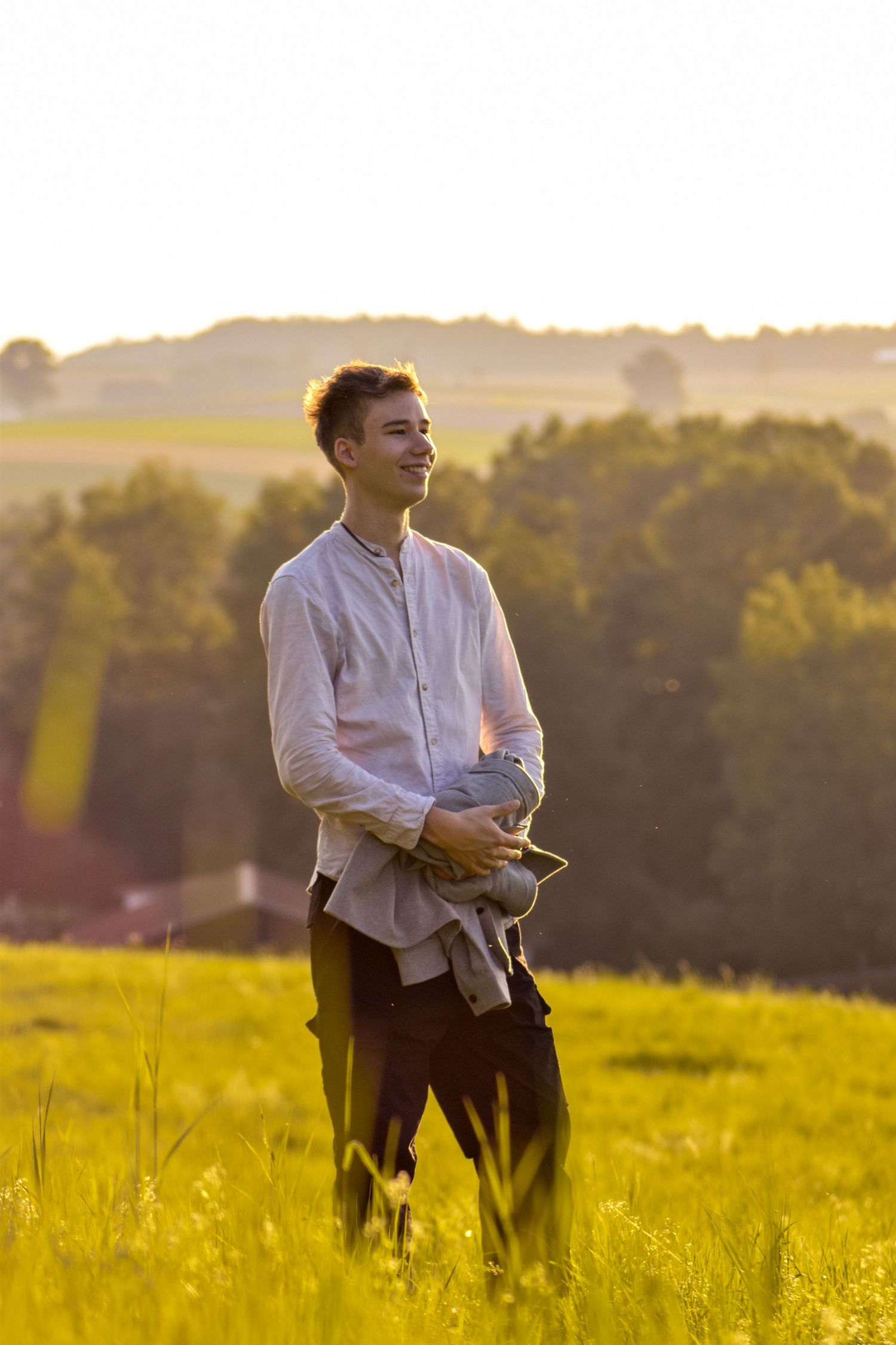 Person standing in golden sunlit meadow during sunset holding jacket.