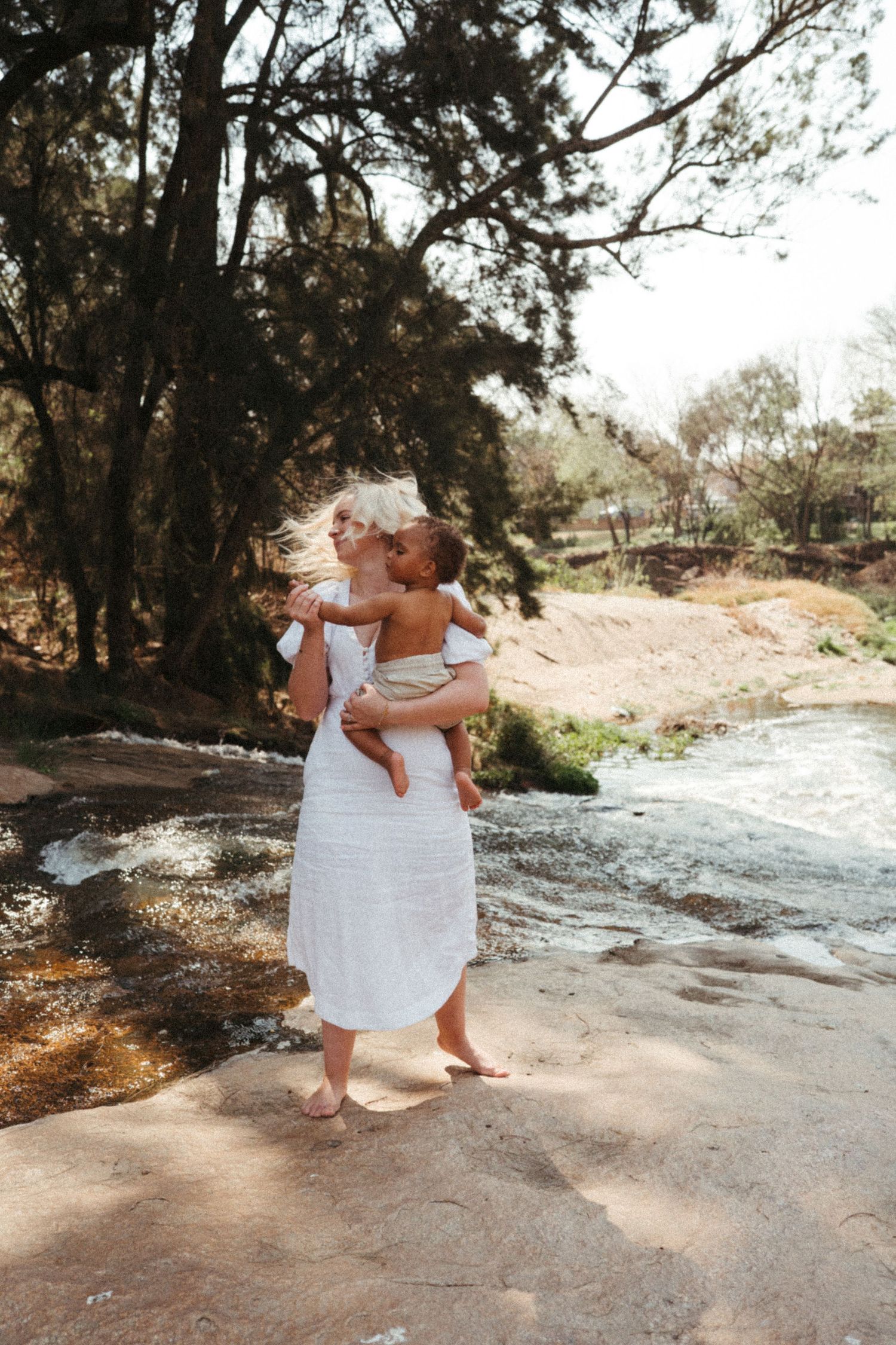 Outdoor photoshoot by flowing water showing intimate moments in natural lighting.