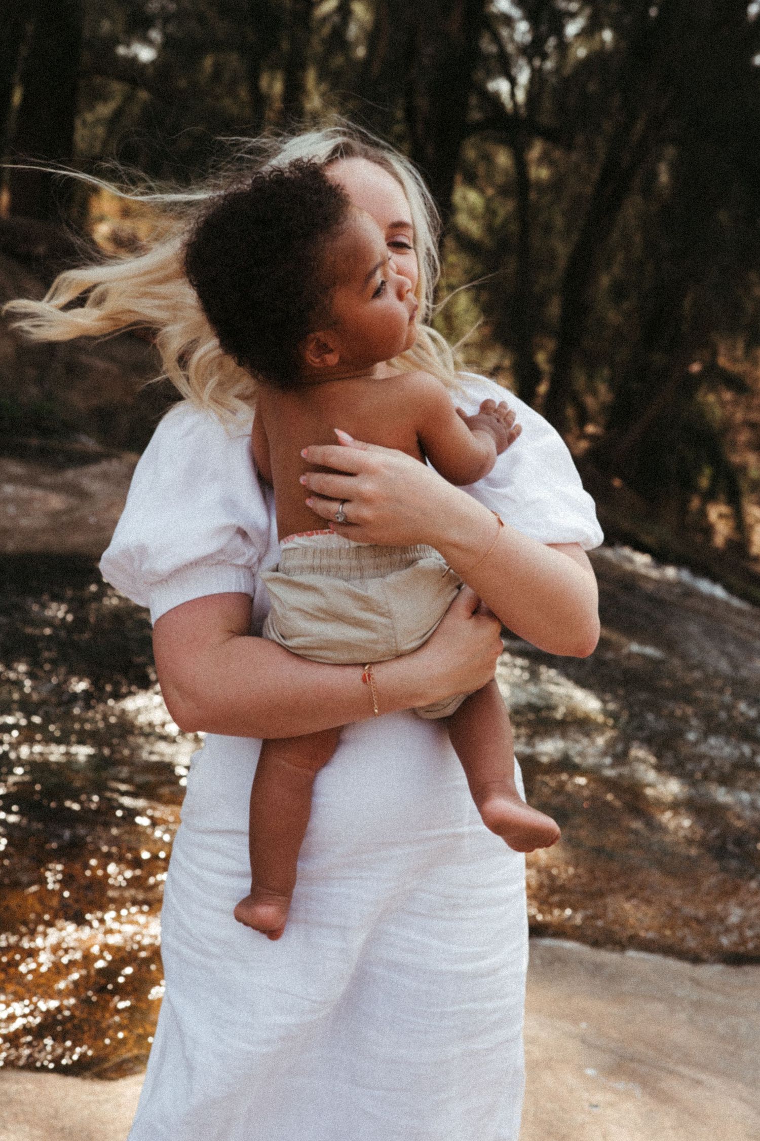 A tender embrace between parent and child in white clothing against a natural outdoor backdrop.