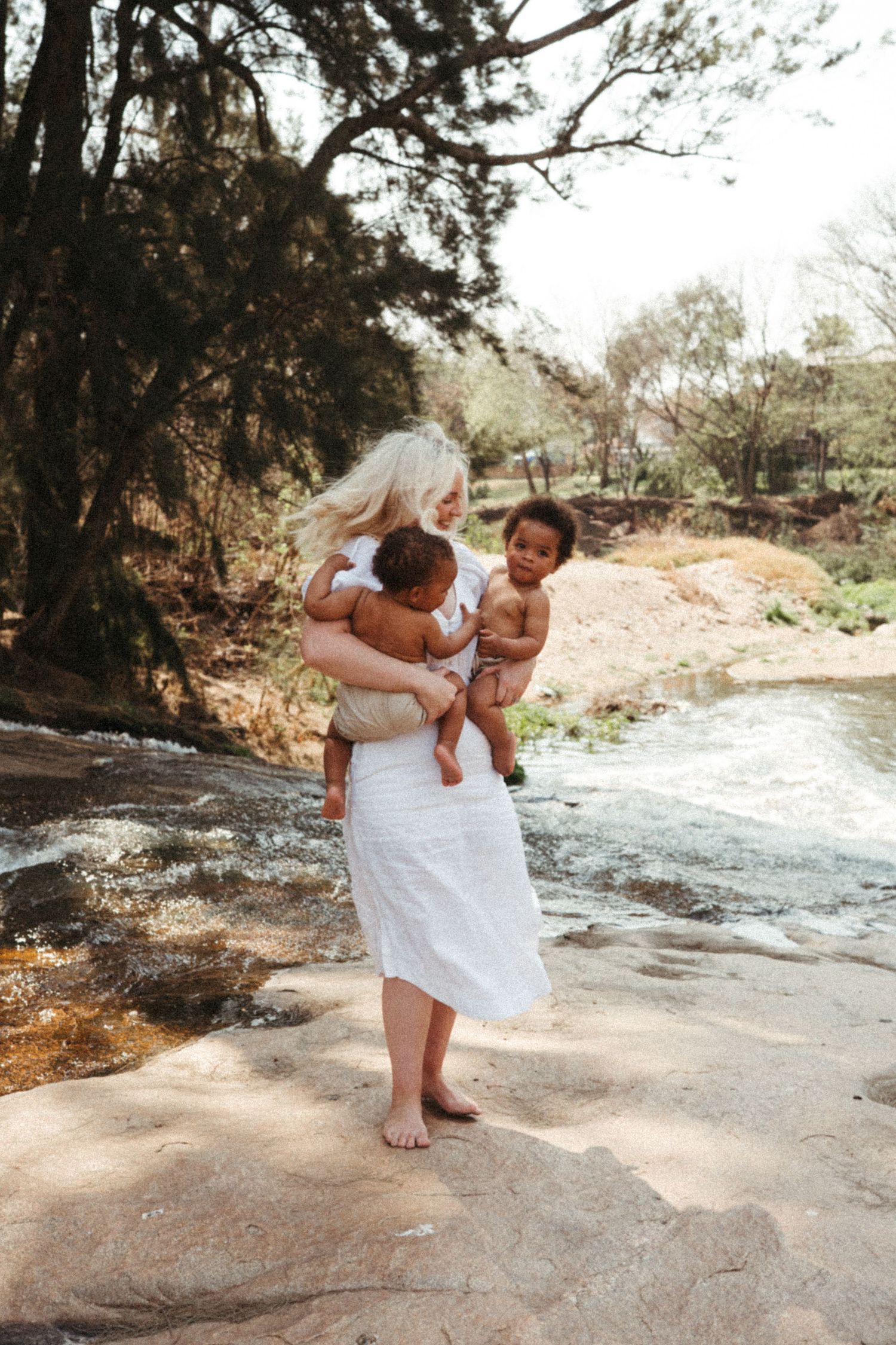 Parent and child playing together on rocky terrain near a stream in white summer outfits.