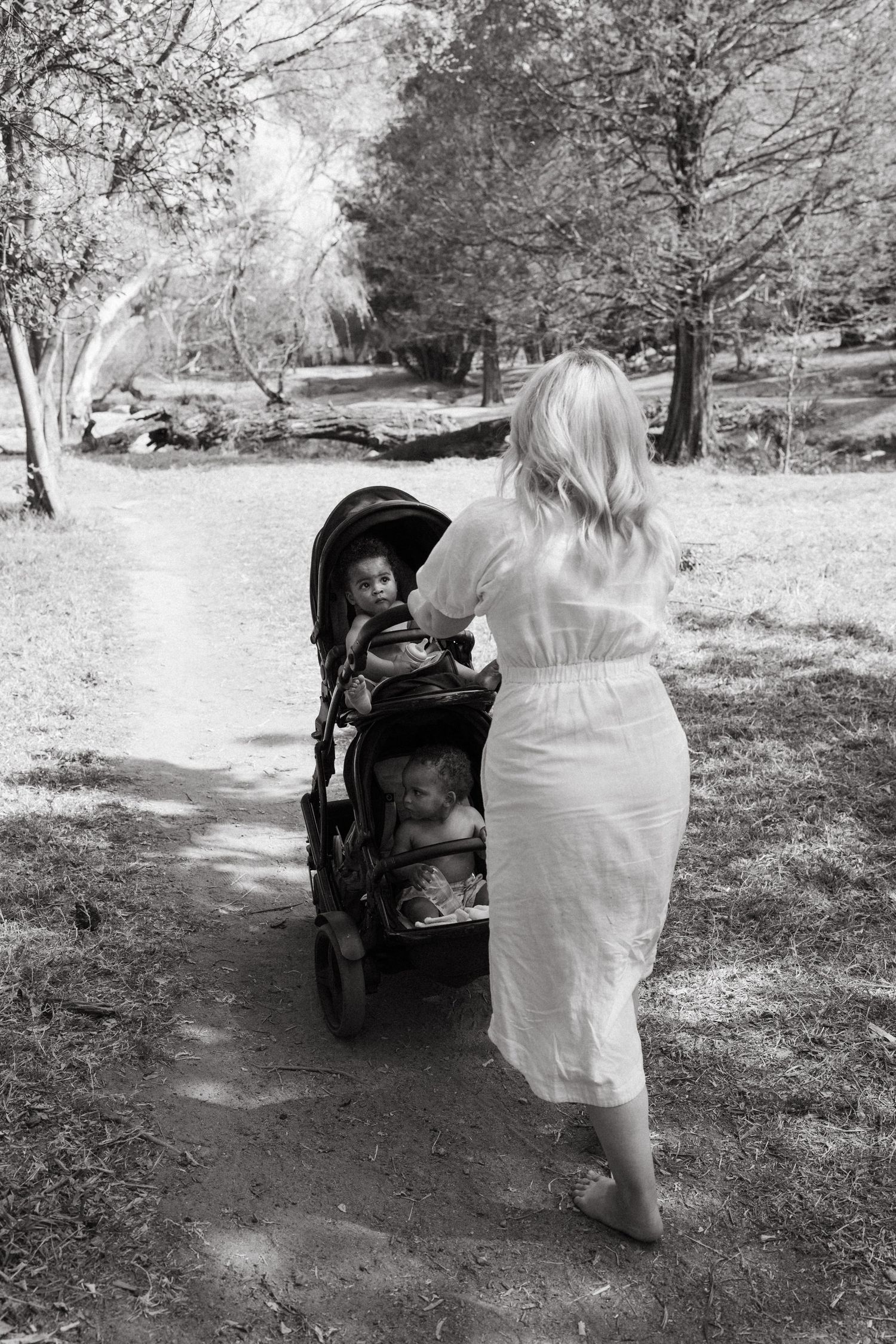 Parent pushing a stroller along a peaceful tree-lined path in white clothing.