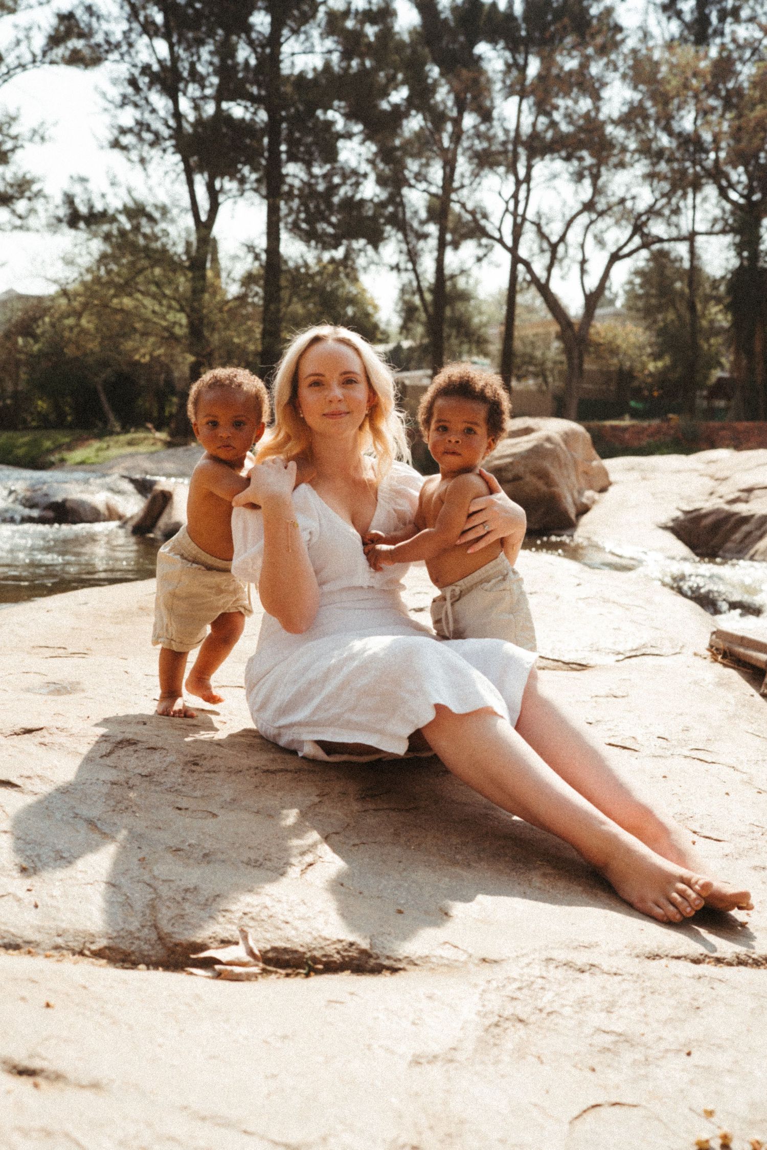 Sun-drenched family portrait on rocky terrain near flowing water.