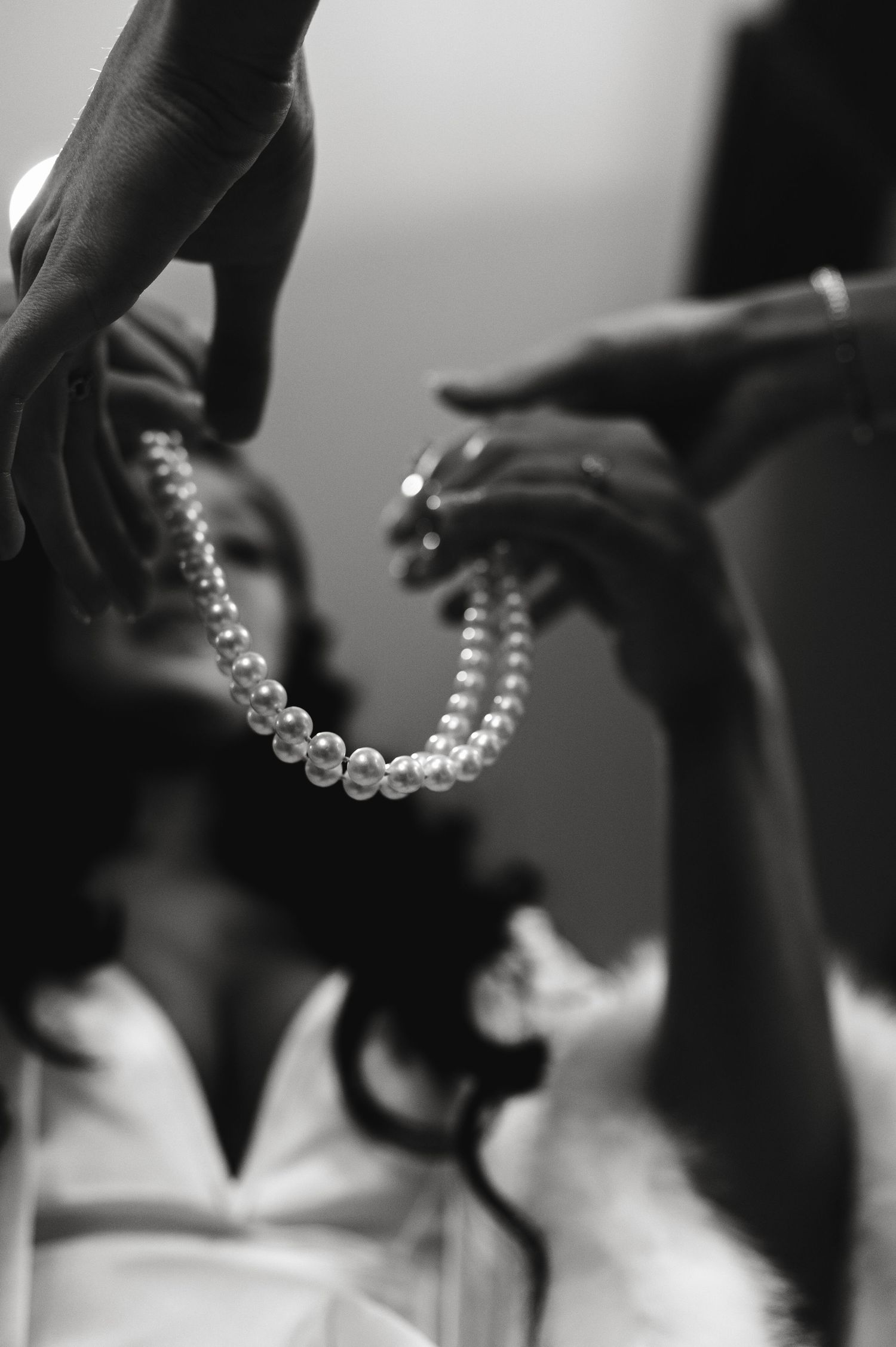 Black and white artistic series showing hands delicately holding a pearl necklace in different positions.