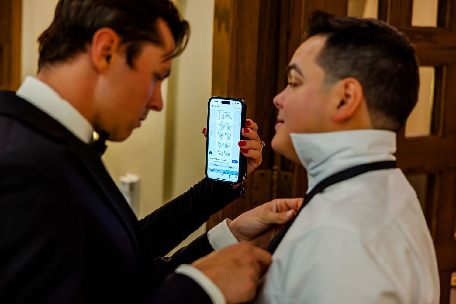 Two people in formal attire examine a smartphone screen displaying text in a wood-paneled room.