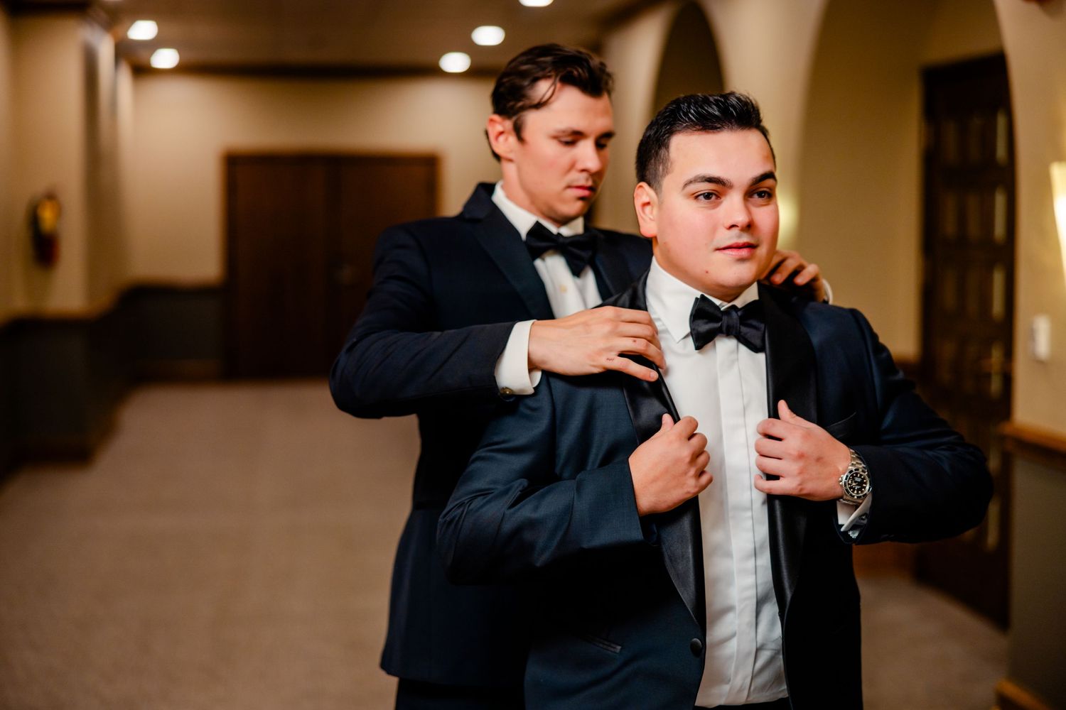 A groom in a black tuxedo adjusts his bowtie while getting ready for his wedding ceremony.