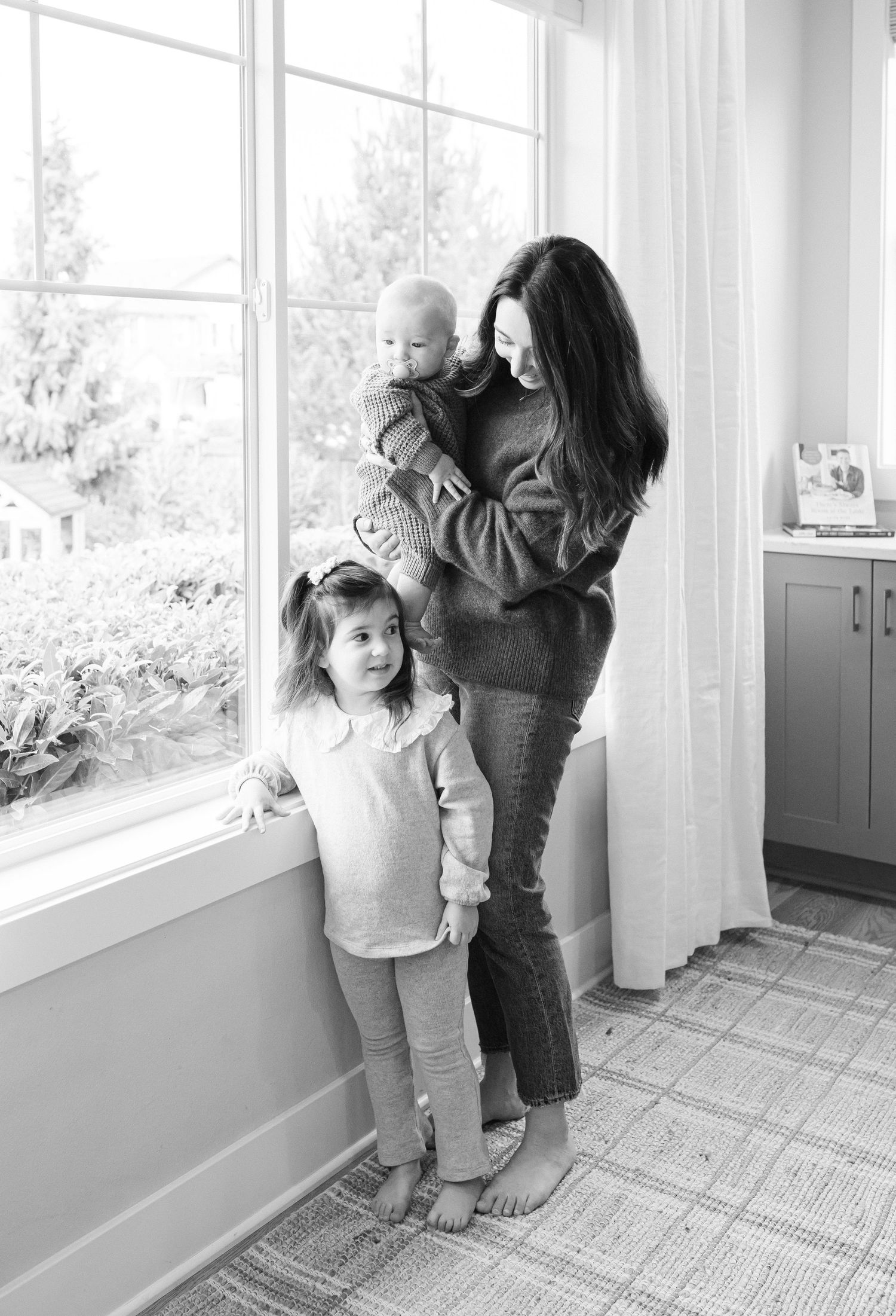A sequence of black and white photos showing parent and child playfully interacting by a sunlit window.