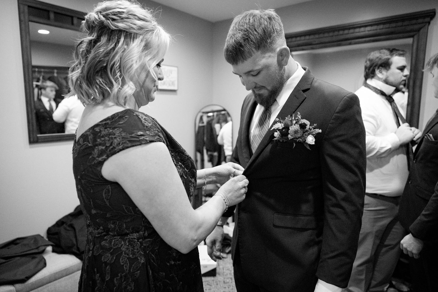 A touching black and white moment shows final preparations before a wedding ceremony in a dressing room.