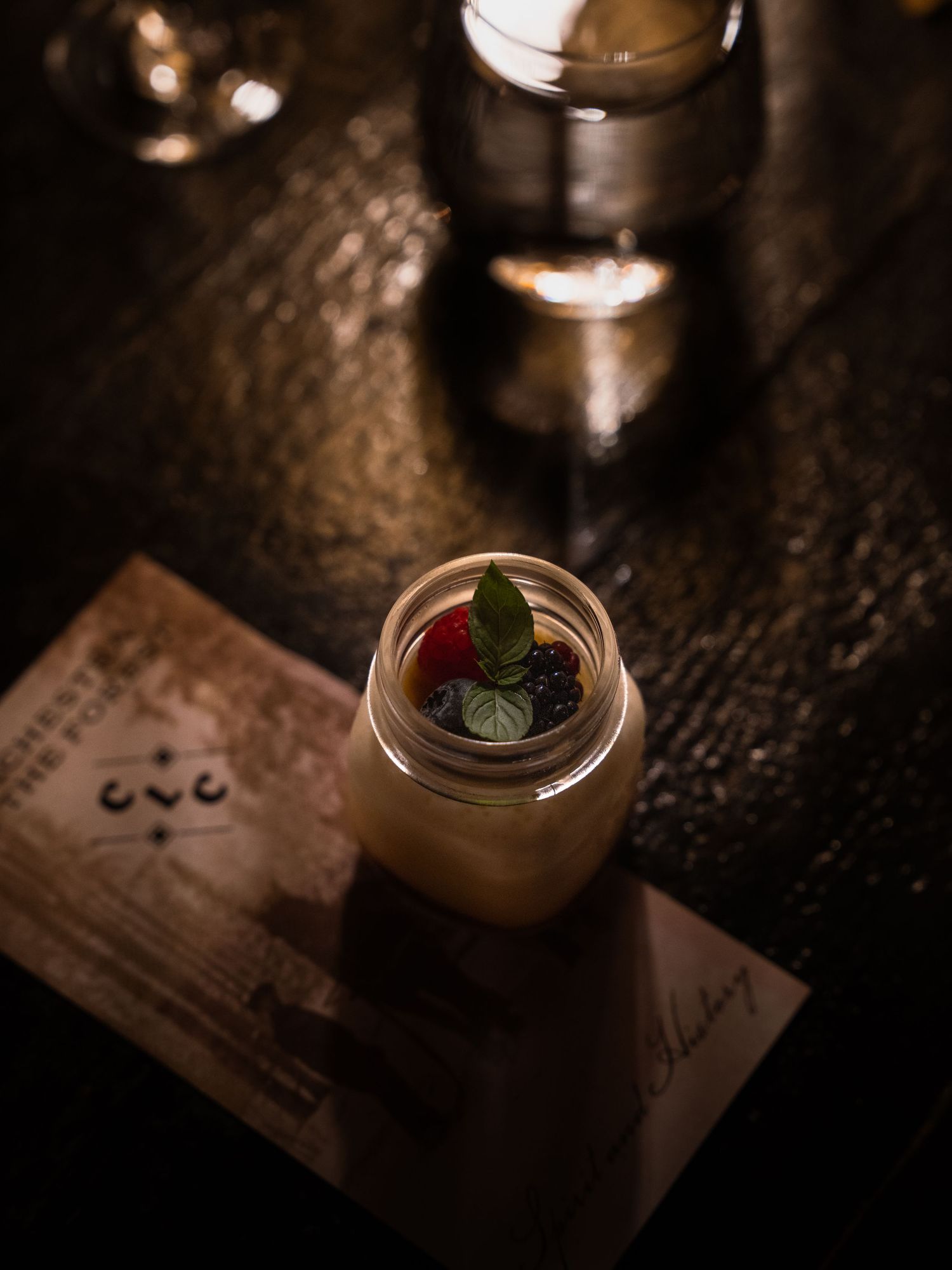 Artisanal cocktail in a mason jar with garnish on a dark wooden table.