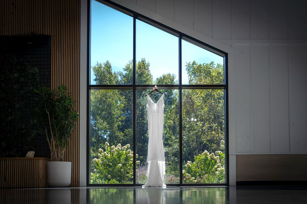 A white wedding dress hangs in front of large windows with natural daylight streaming in Columbus Ohio showcasing a venue