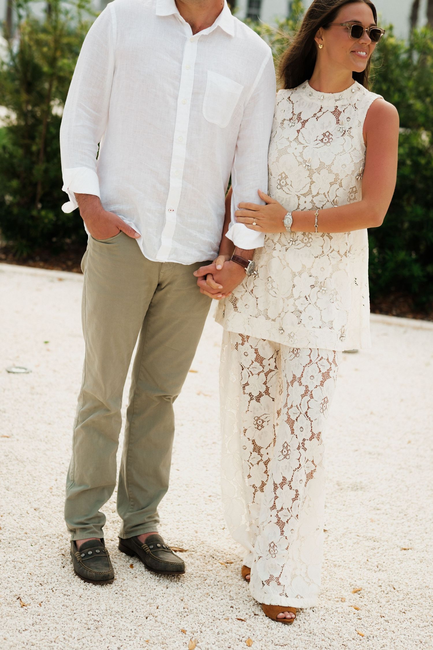 A couple in matching white outfits holding hands on a sunny day.