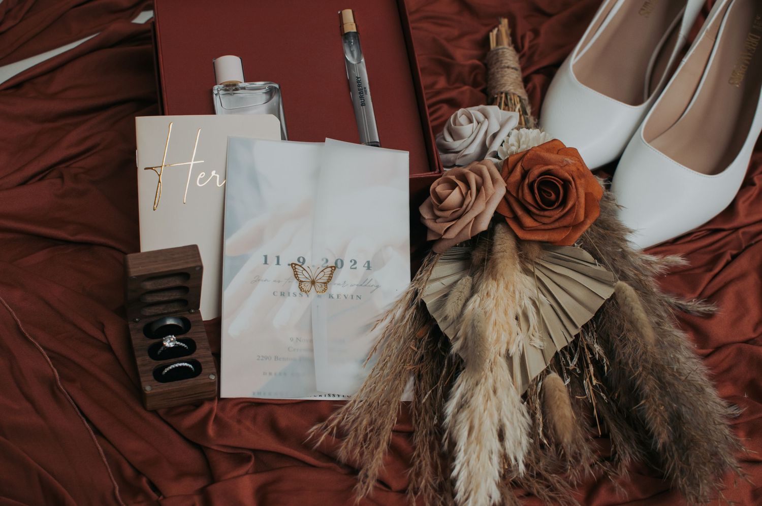 Wedding details including vow books and decorative elements styled on burgundy fabric.