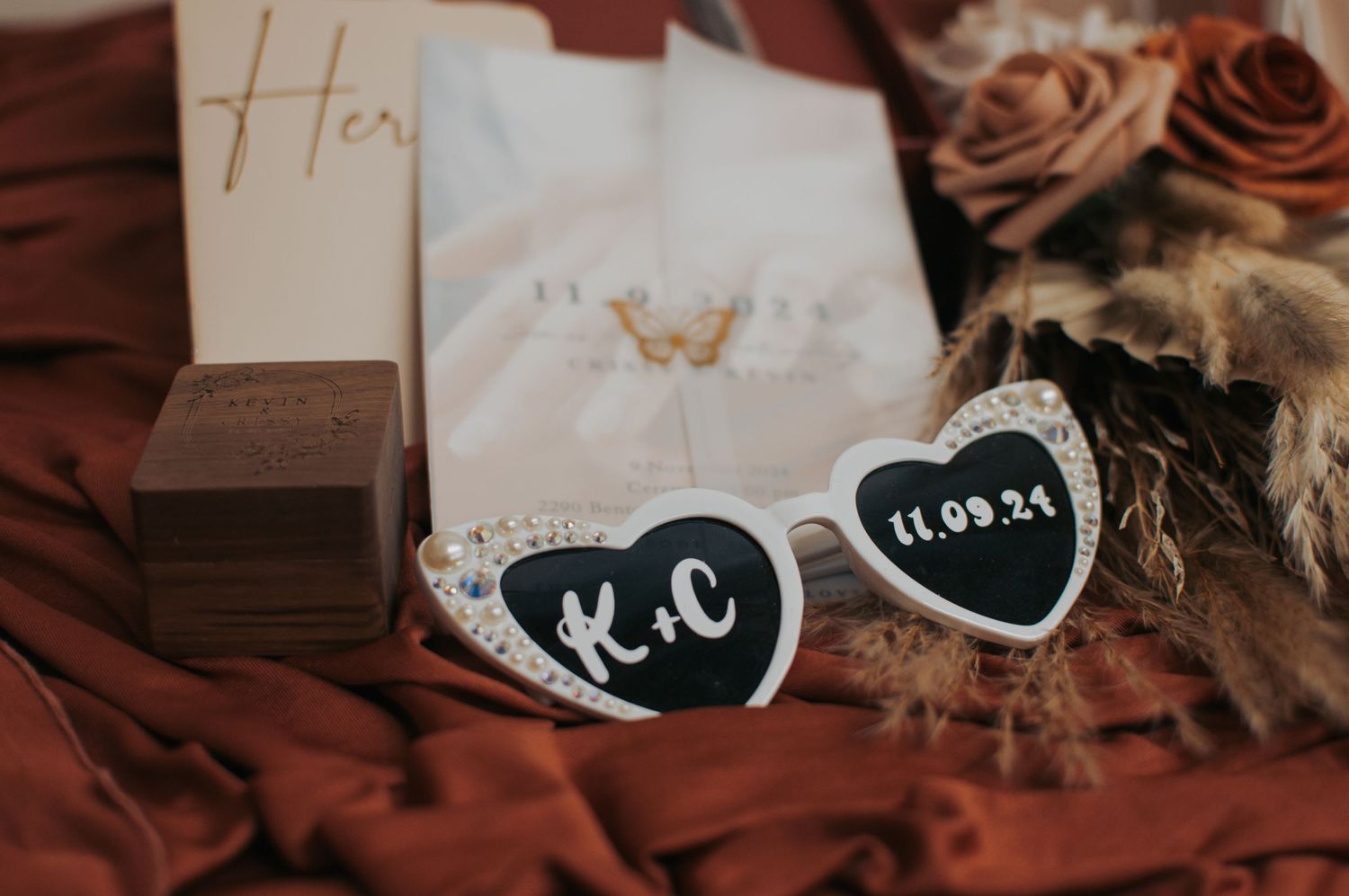 Wedding stationery and vow books arranged with roses on dark fabric.