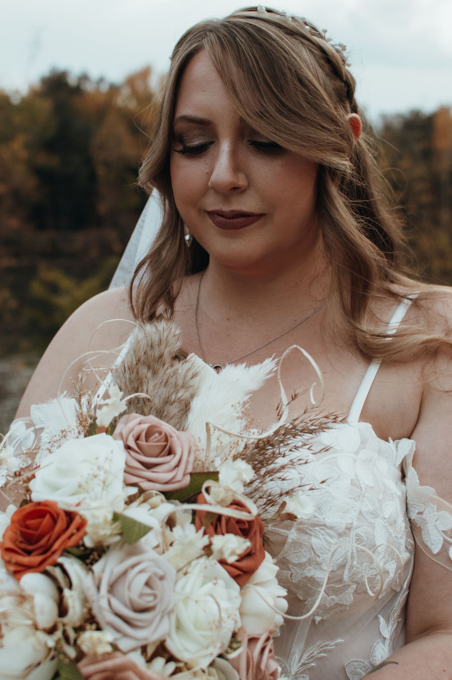 Bride holding romantic bouquet of blush and rust roses with white flowers.