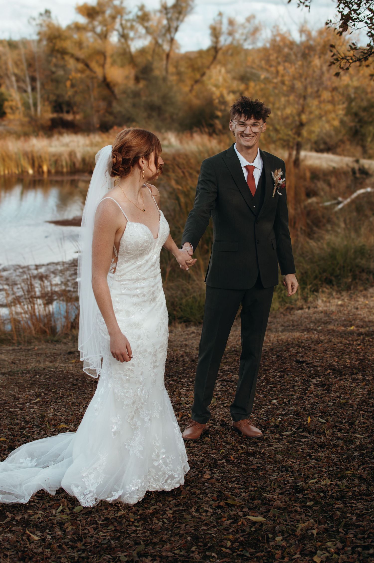 Wedding couple poses by a scenic lake during autumn season.