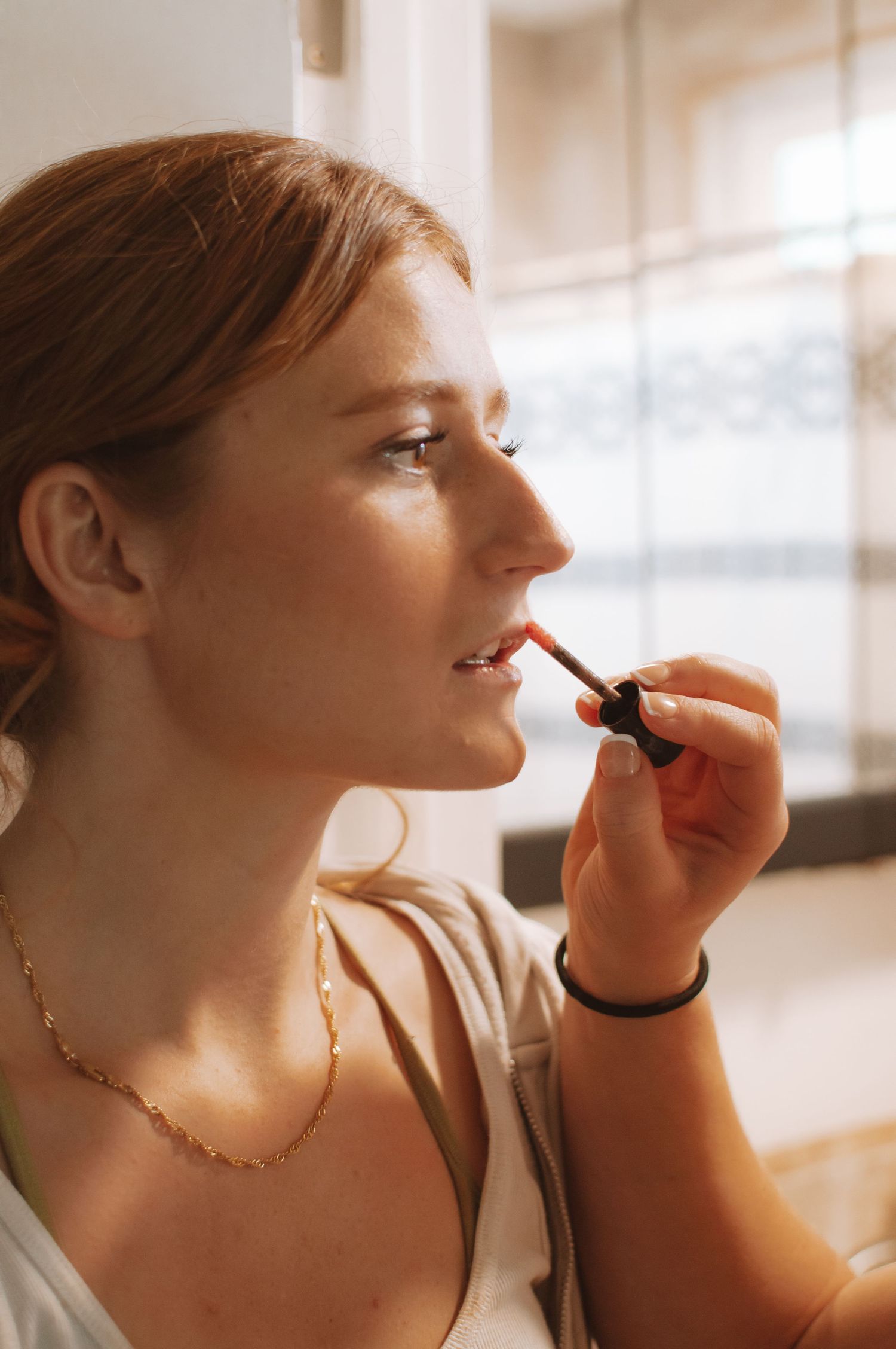 Side profile of someone applying lipstick in natural window light.