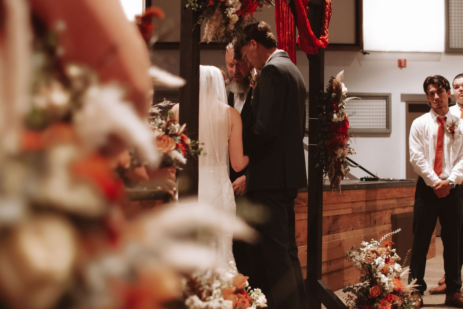 Indoor wedding ceremony setup with red floral decorations.