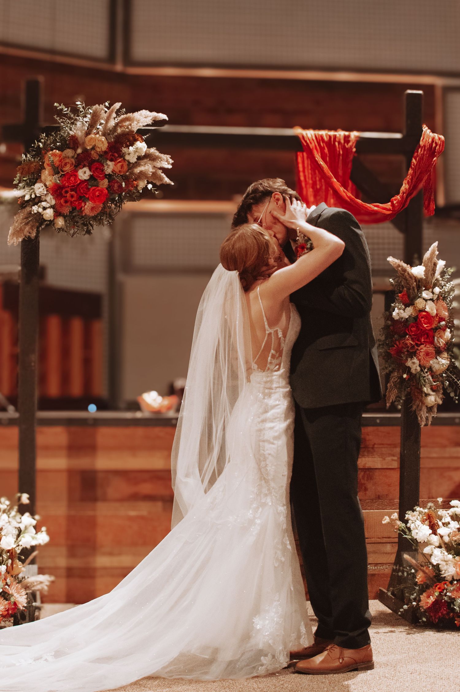 Wedding ceremony at indoor venue with red floral arch decorations and flowing white wedding dress.