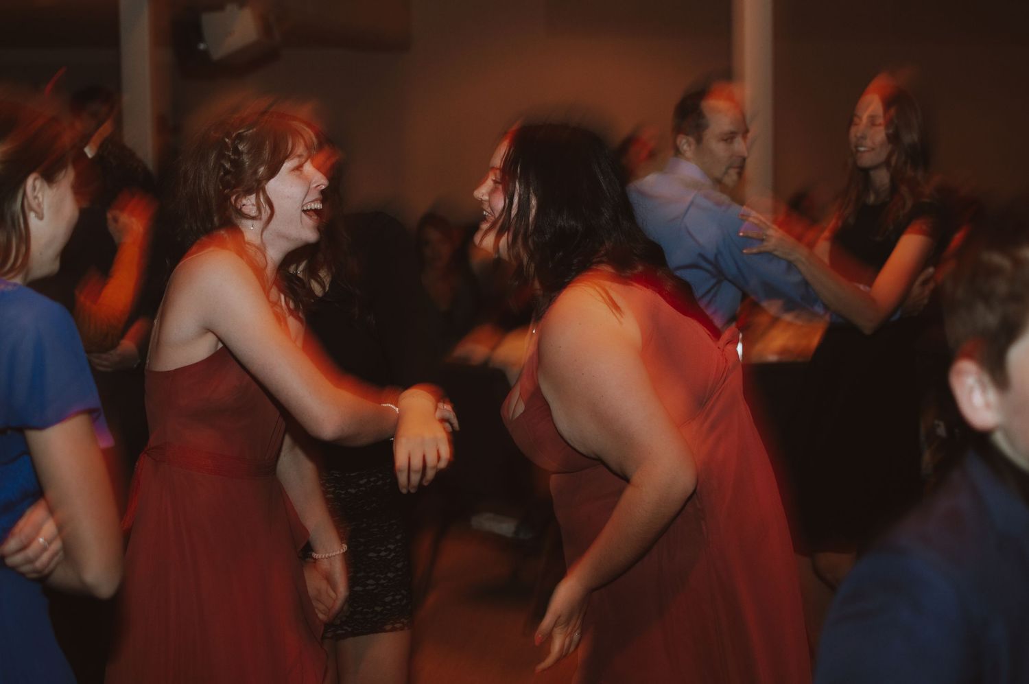 Wedding guests dancing energetically at reception in red ambient lighting.