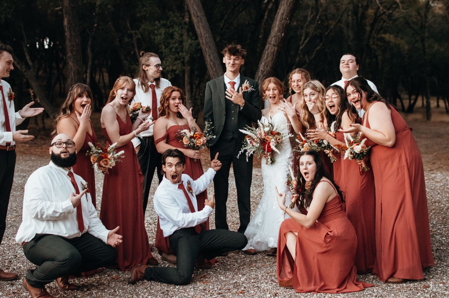 Wedding party group photo with bridesmaids in rust-colored dresses.