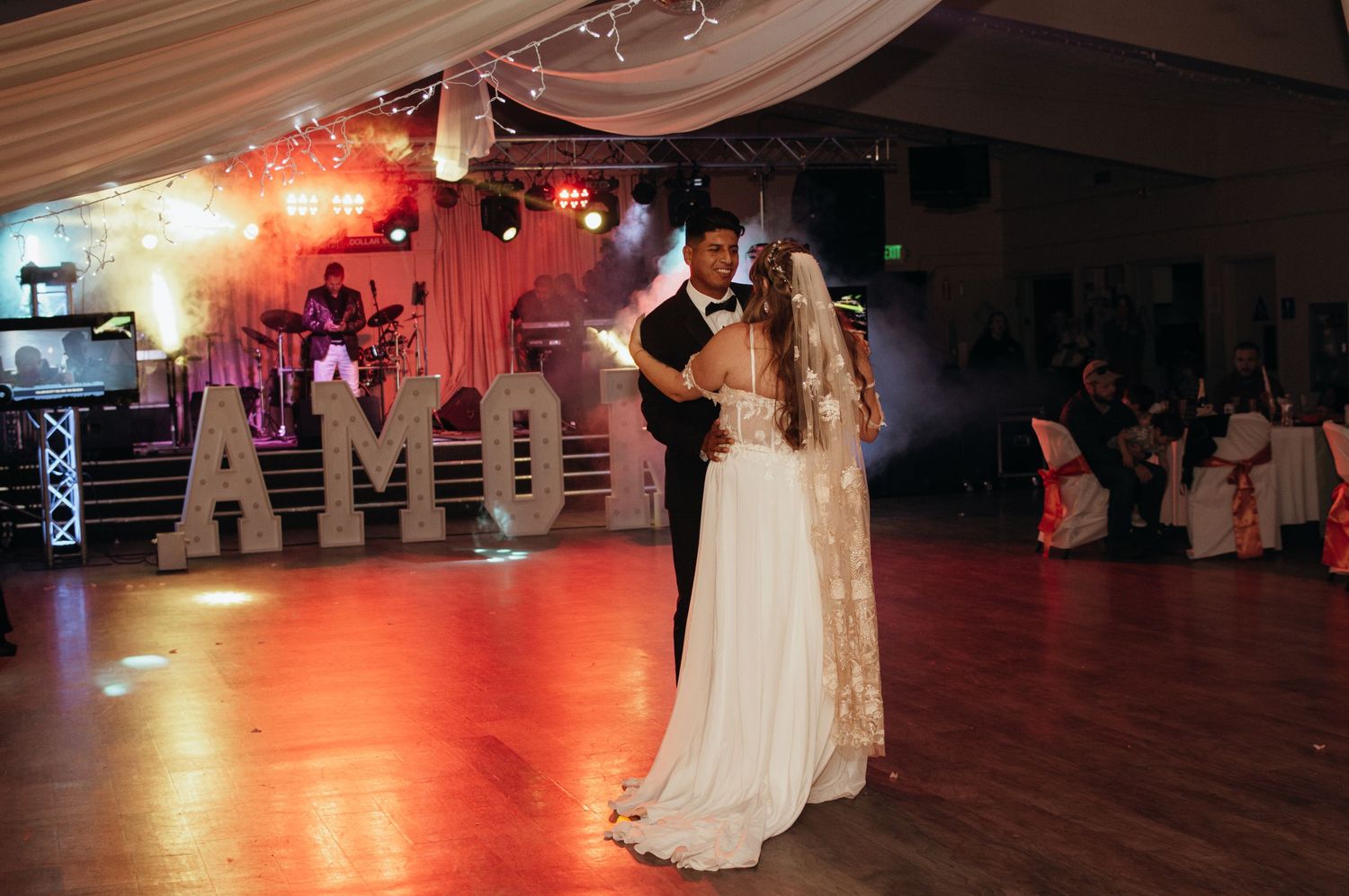 Wedding reception venue with string lights and couples dancing on hardwood floor.