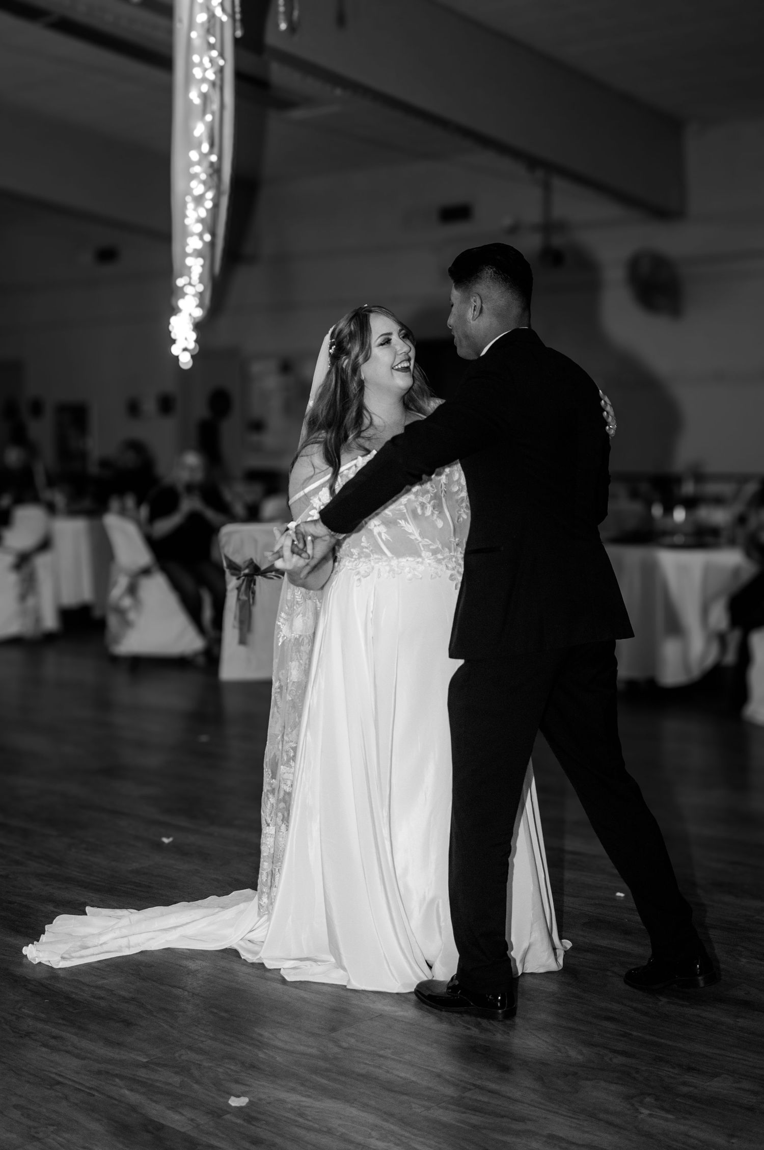 Black and white photo of a wedding dance scene on a wooden ballroom floor.