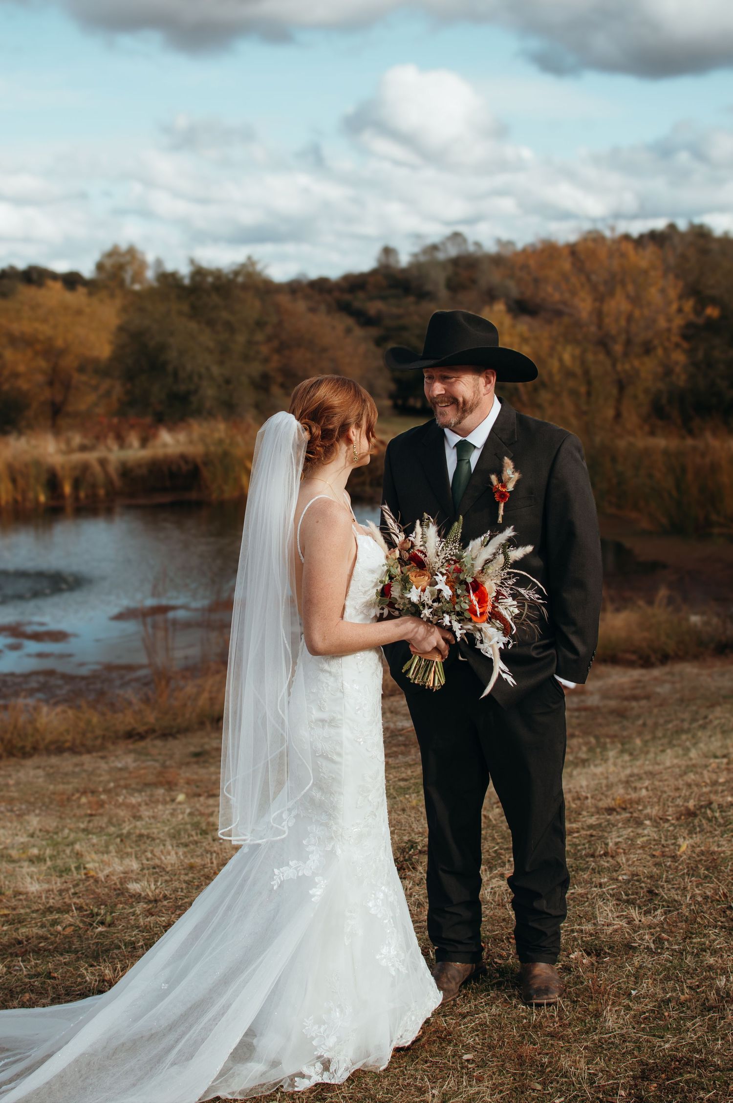 Wedding portrait with bride holding rustic bouquet by autumn lake.