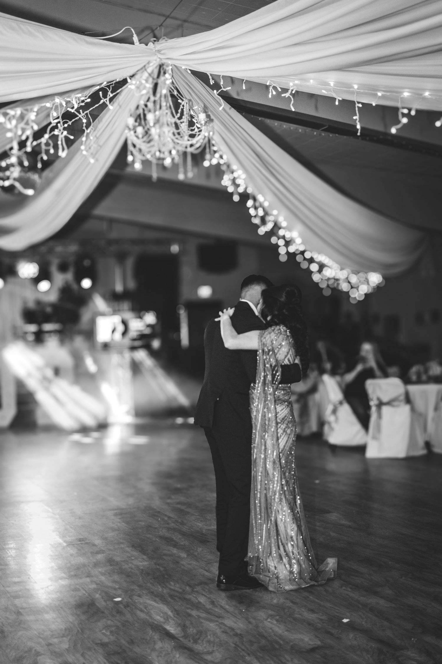 Monochrome wedding reception photo showing dancing under draped fabric and string lights.