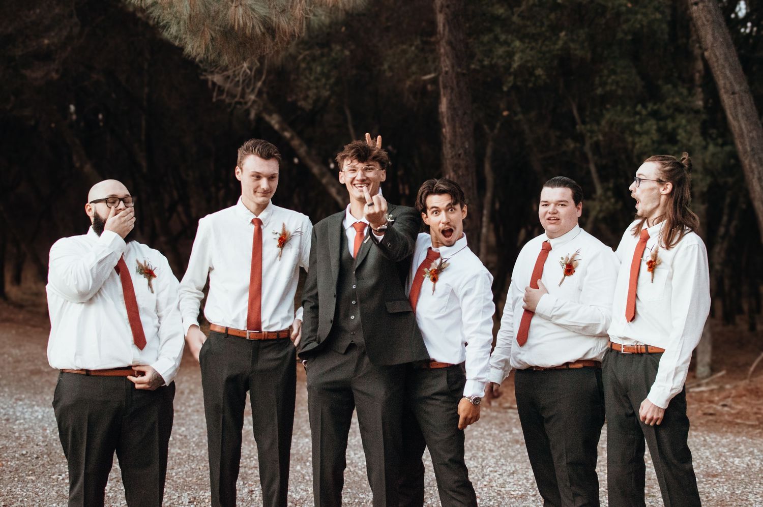 Groomsmen in white shirts and red ties pose playfully for camera.
