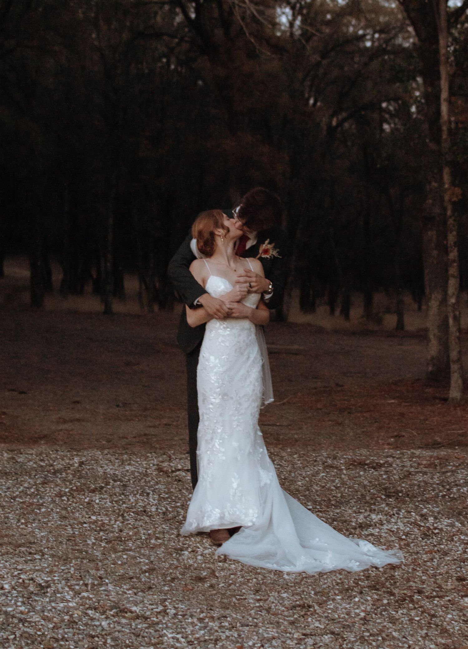 Romantic wedding couple embraces during sunset photoshoot on autumn grounds with fallen leaves.