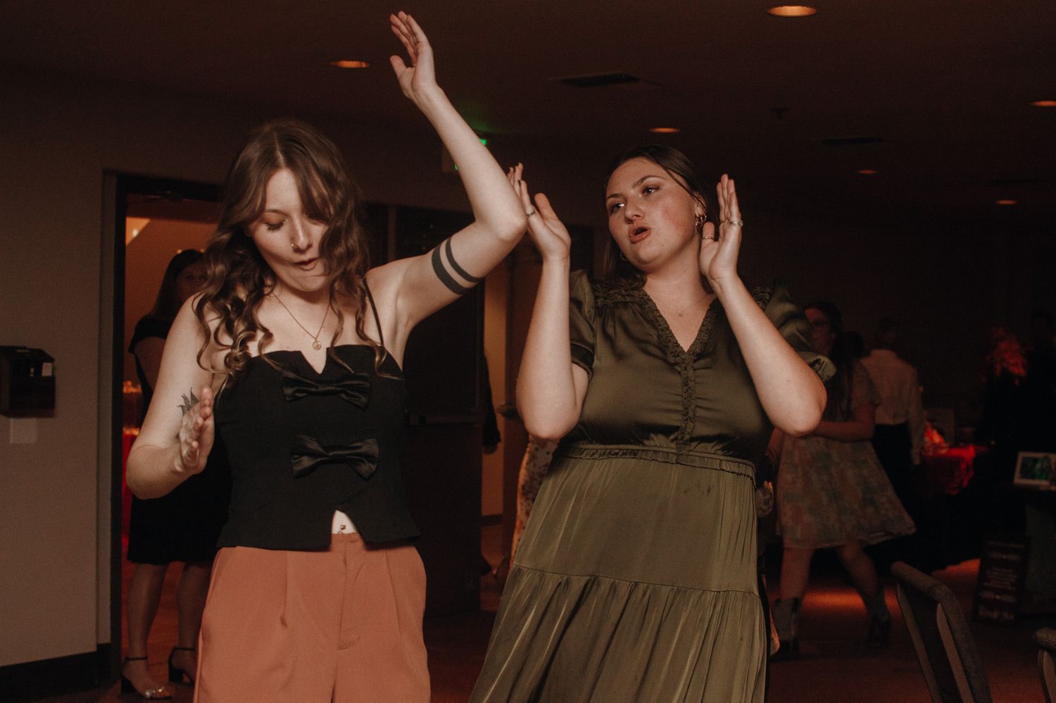 Wedding party guests dance and celebrate on a dimly lit dance floor during evening reception festivities.