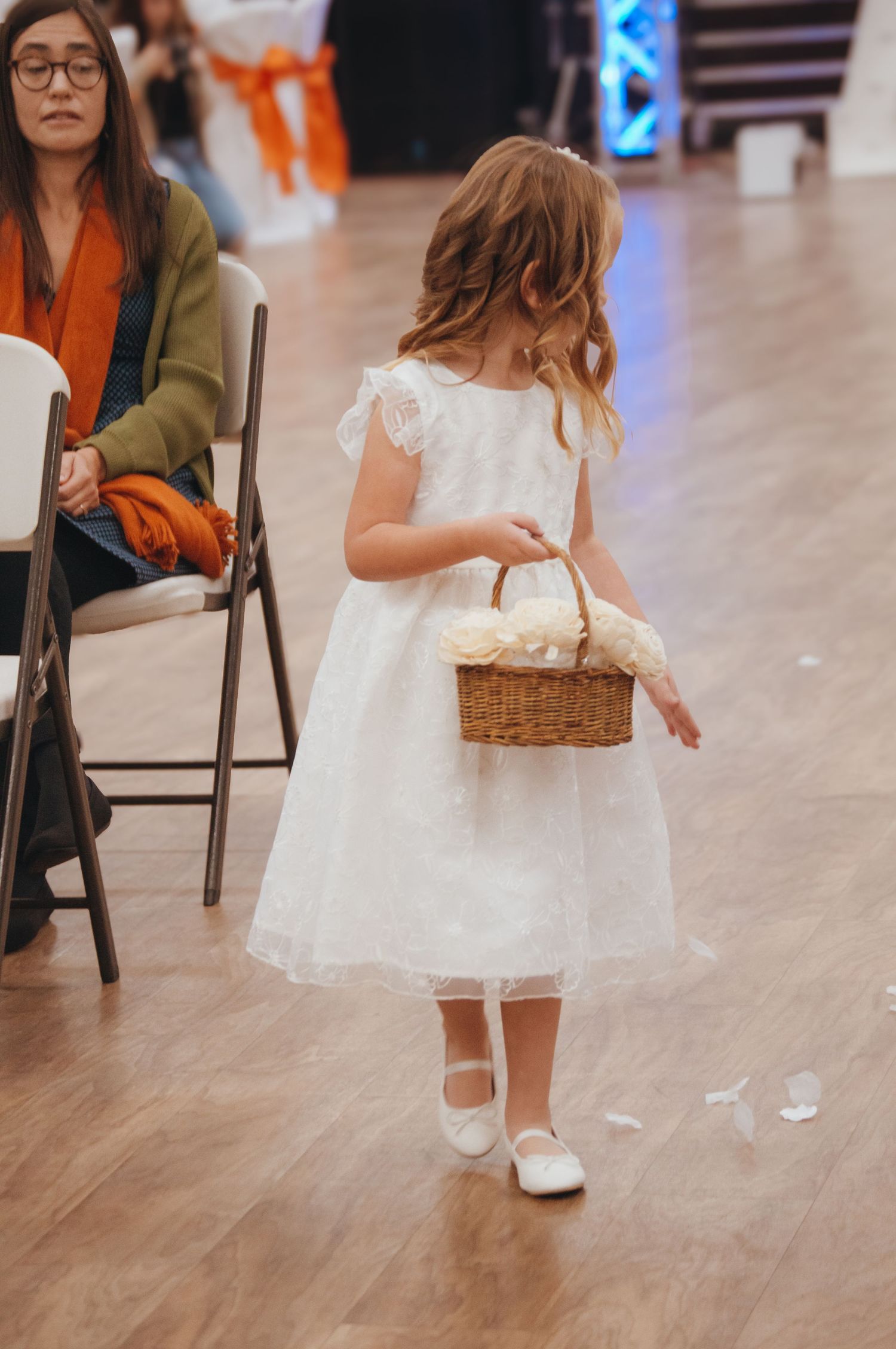 Flower girls in white dresses walk across wooden floor during wedding celebration.
