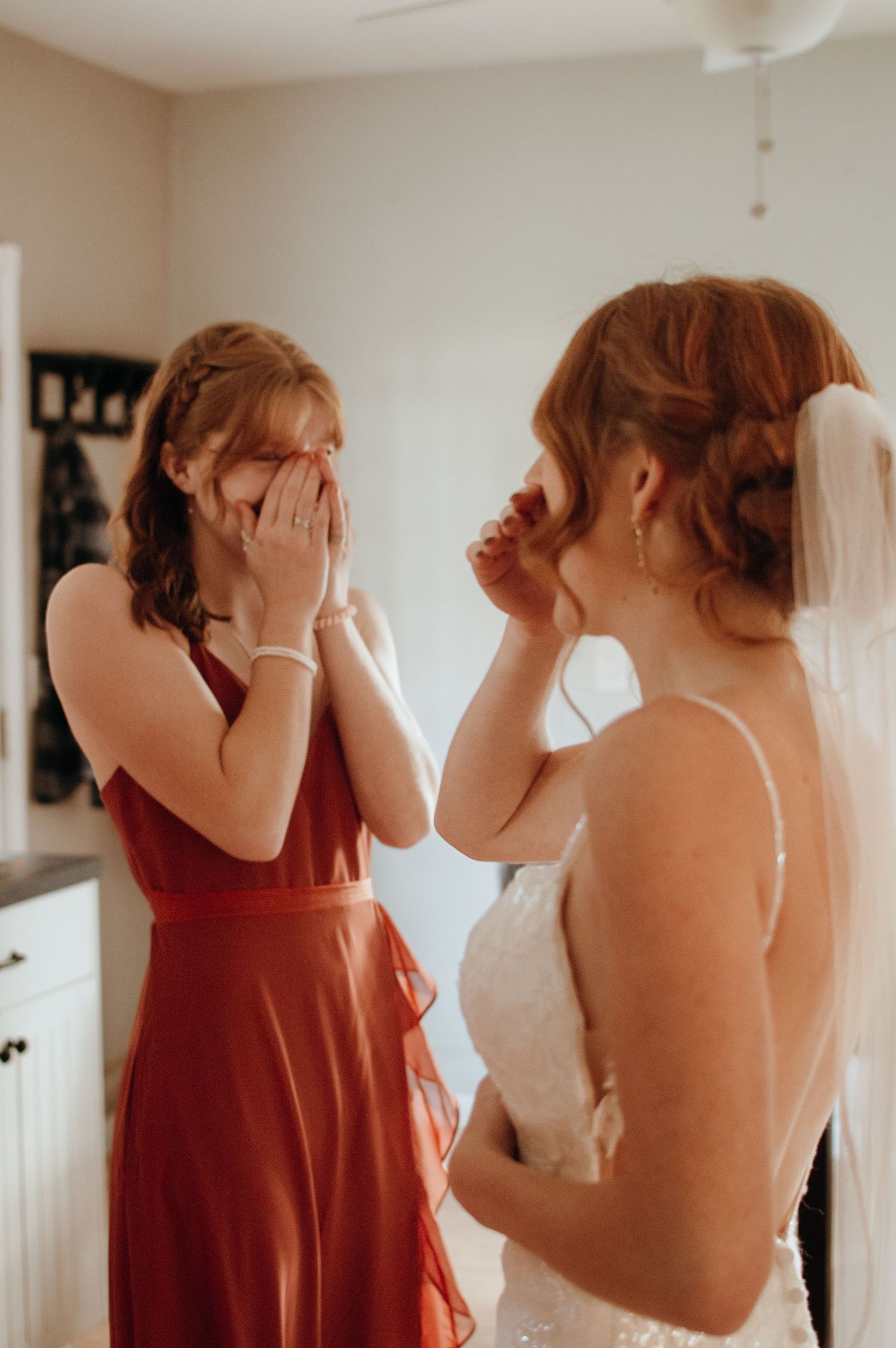 Emotional getting ready moment between bride in white dress and person in burgundy dress.