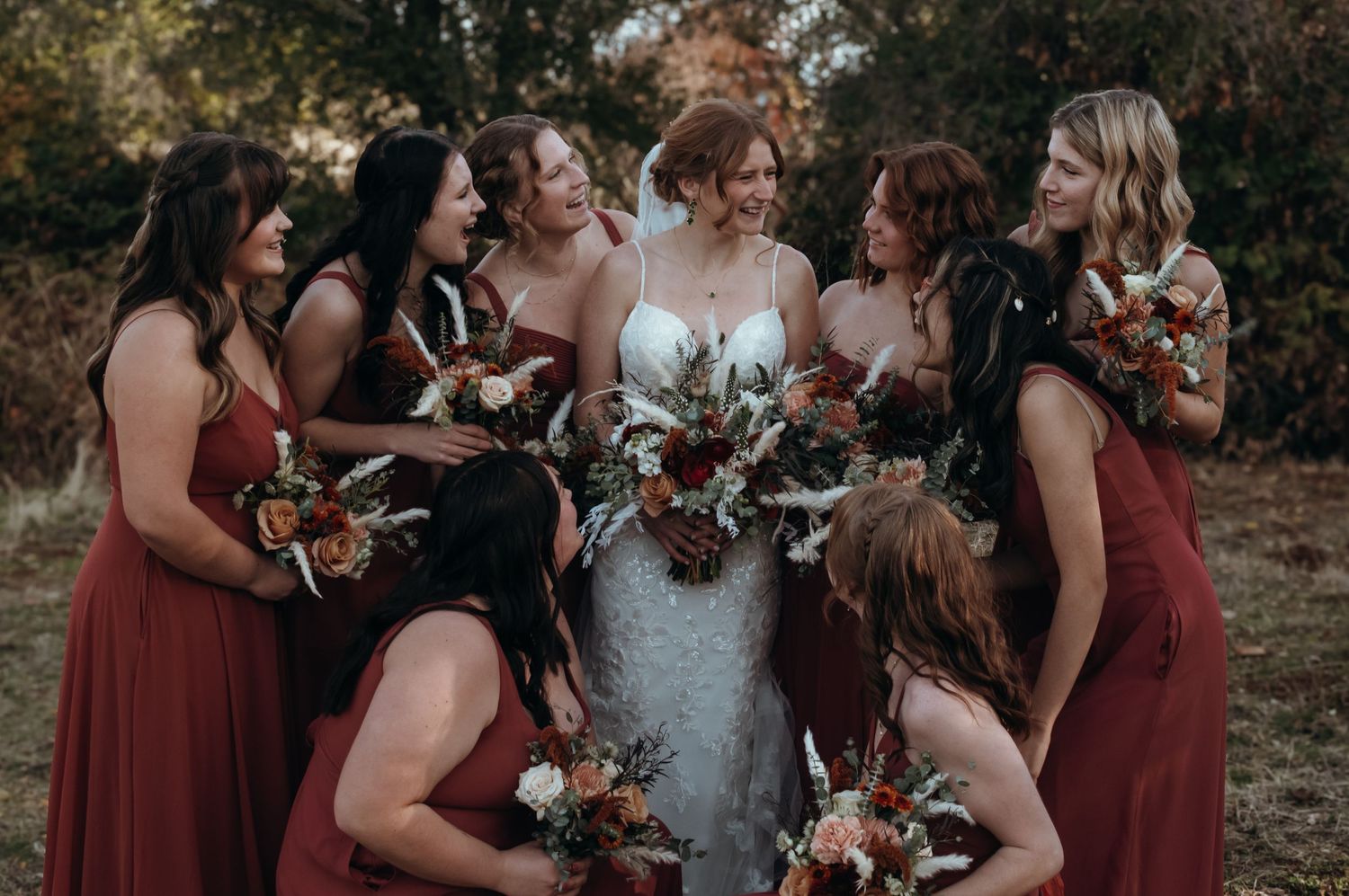Wedding party in burgundy dresses poses together outdoors during autumn celebration.