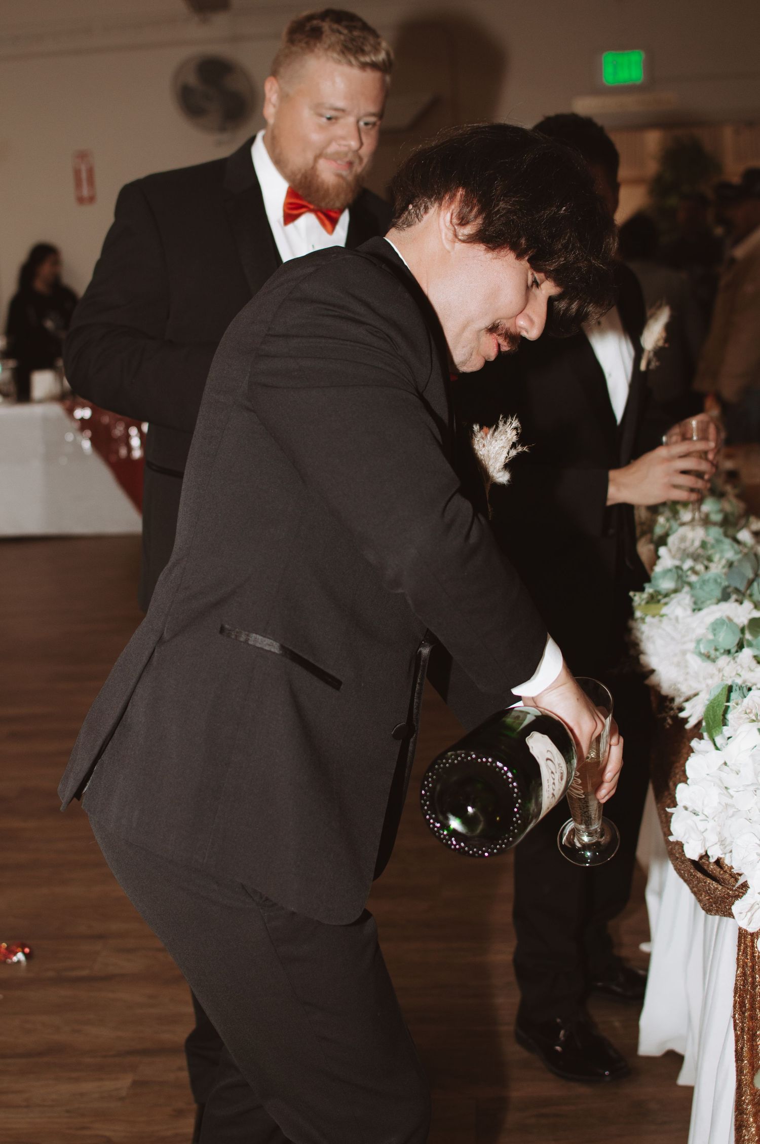 Groomsmen in formal attire pour drinks at a wedding reception.