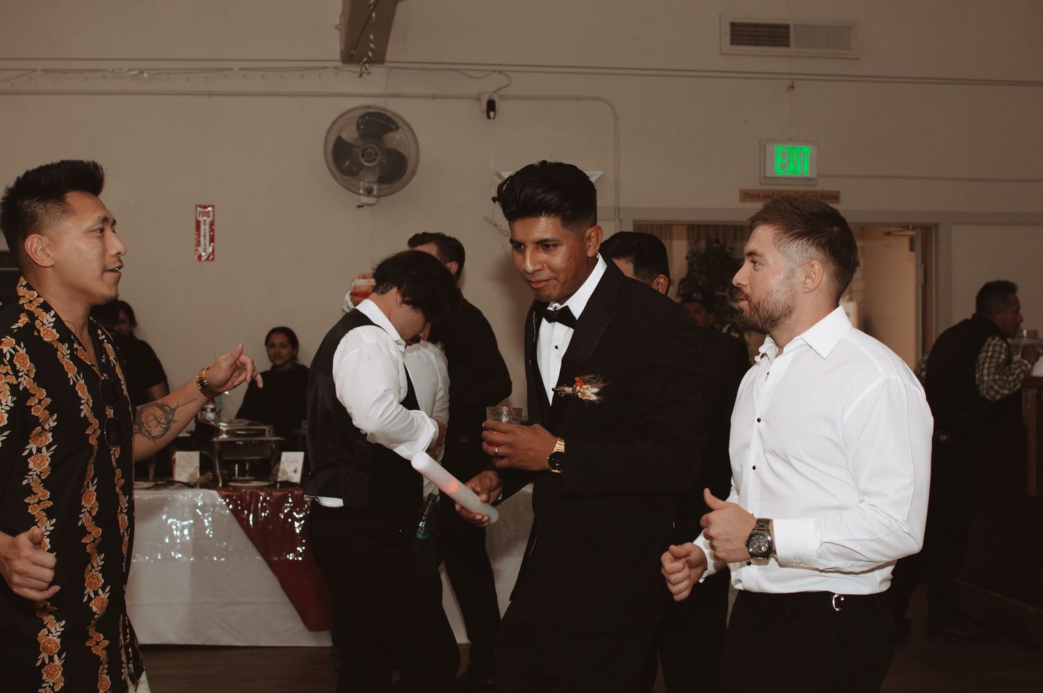 Wedding reception guests dancing and celebrating on a dimly lit dance floor with decorative lights.
