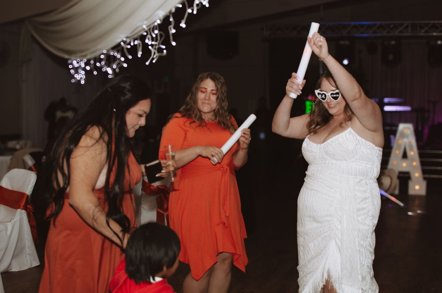 Wedding reception dance party with guests in orange and white outfits.