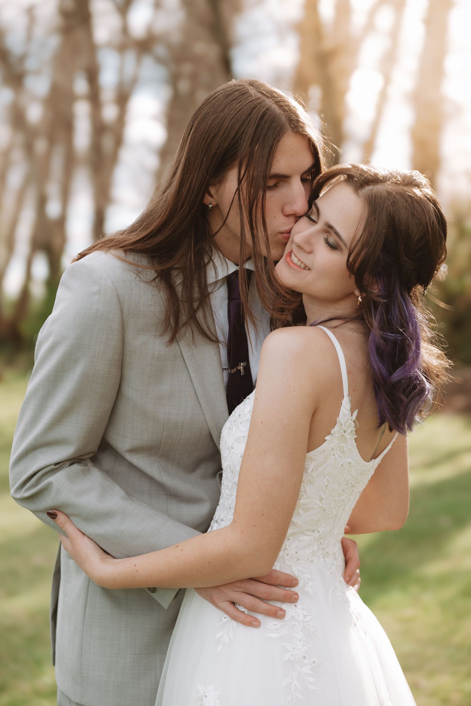 Romantic outdoor portrait of couple embracing in sunlit wooded setting.